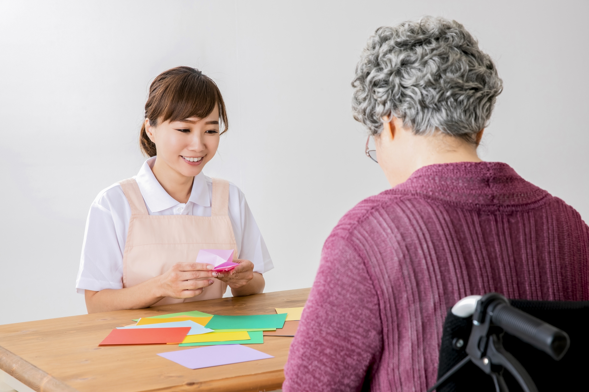 折り紙でレクリエーションする介護士と高齢者の女性