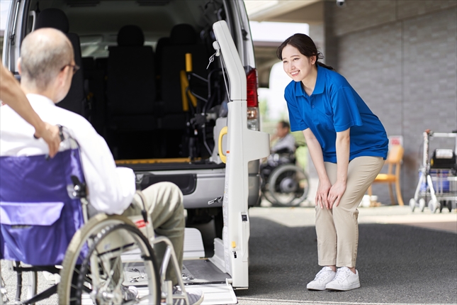 送迎車に乗る高齢者を見送る介護士
