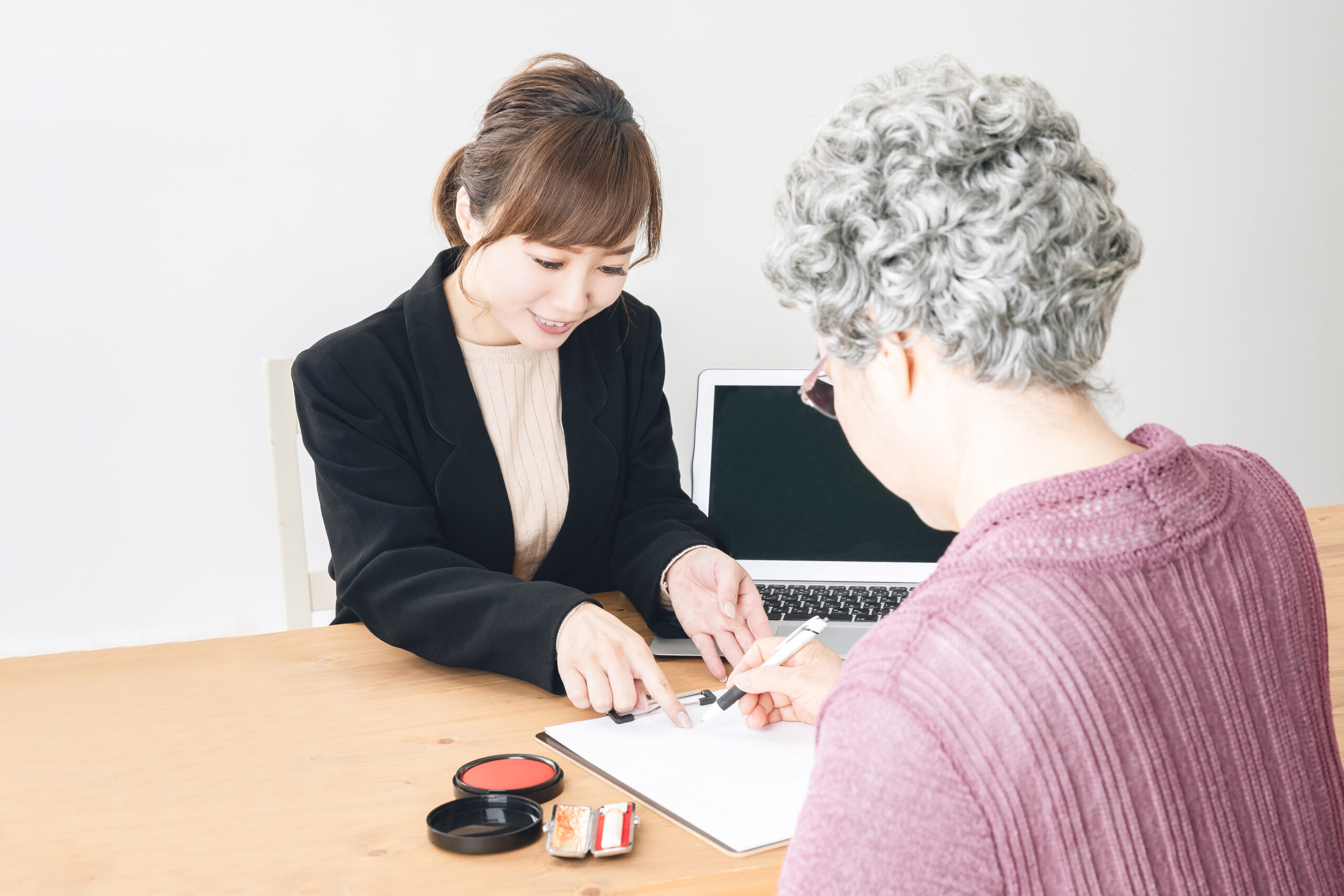 スーツ姿の女性と書類にサインする高齢者