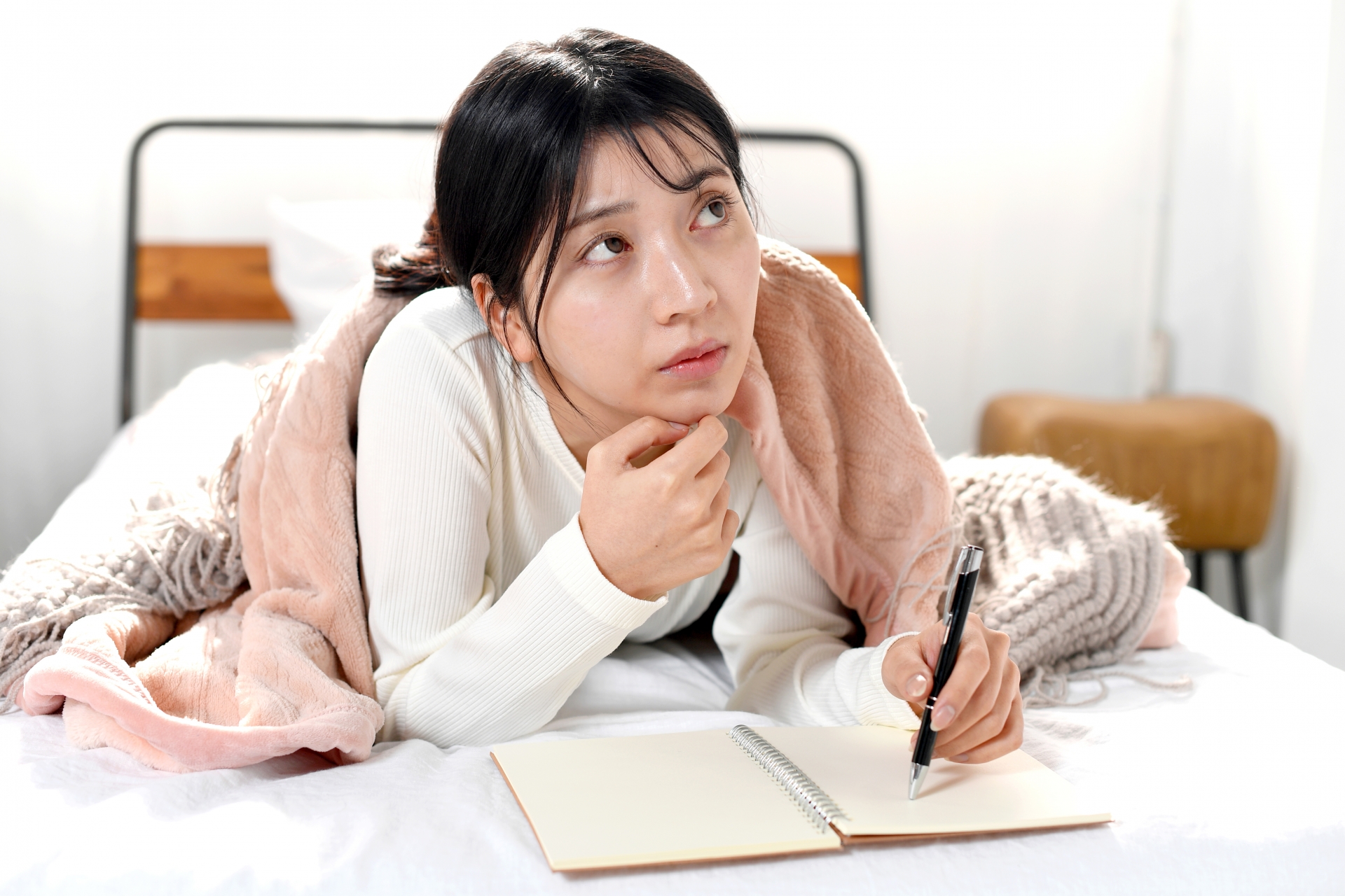 ベッドの上でメモを書き考える若い女性