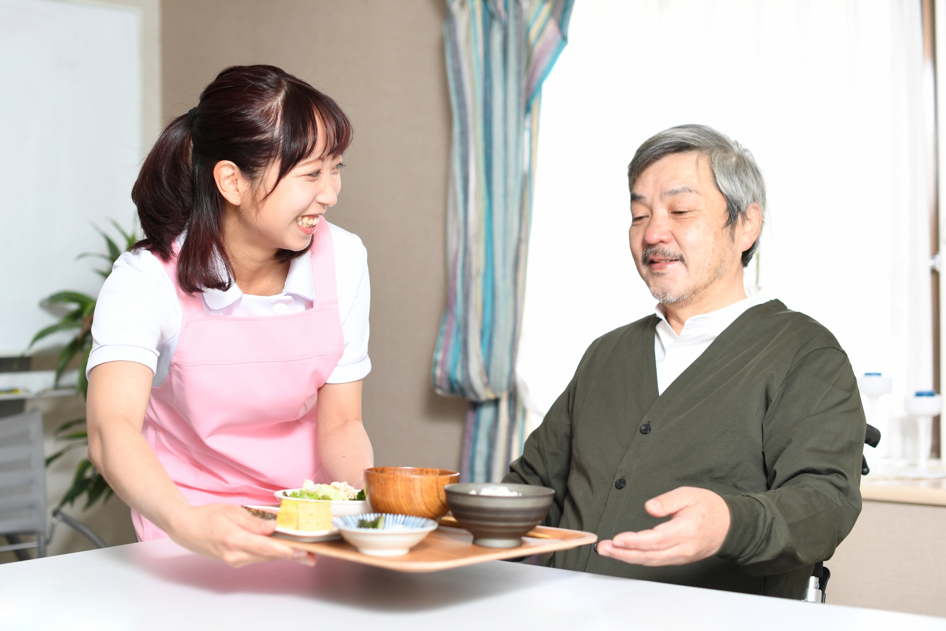 食事を運ぶ女性介護士と高齢者の白髪男性