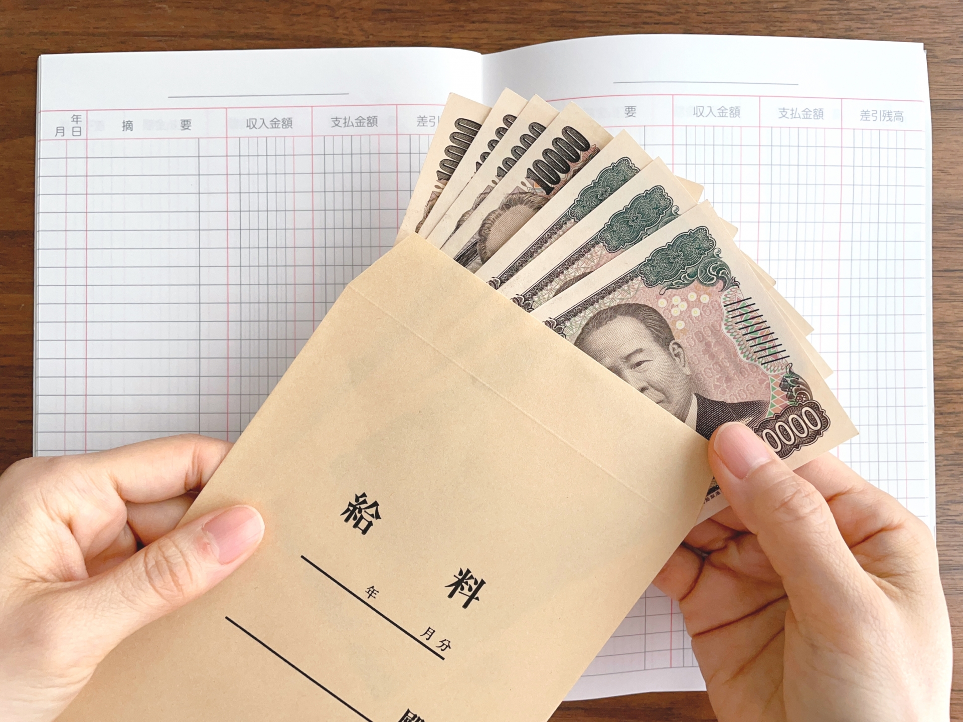 机上の家計簿と給料袋から紙幣を取り出す手