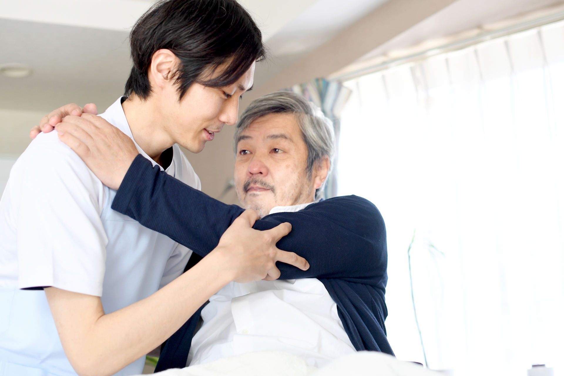 ベッドでお年寄りの男性を起こす介護士の先生