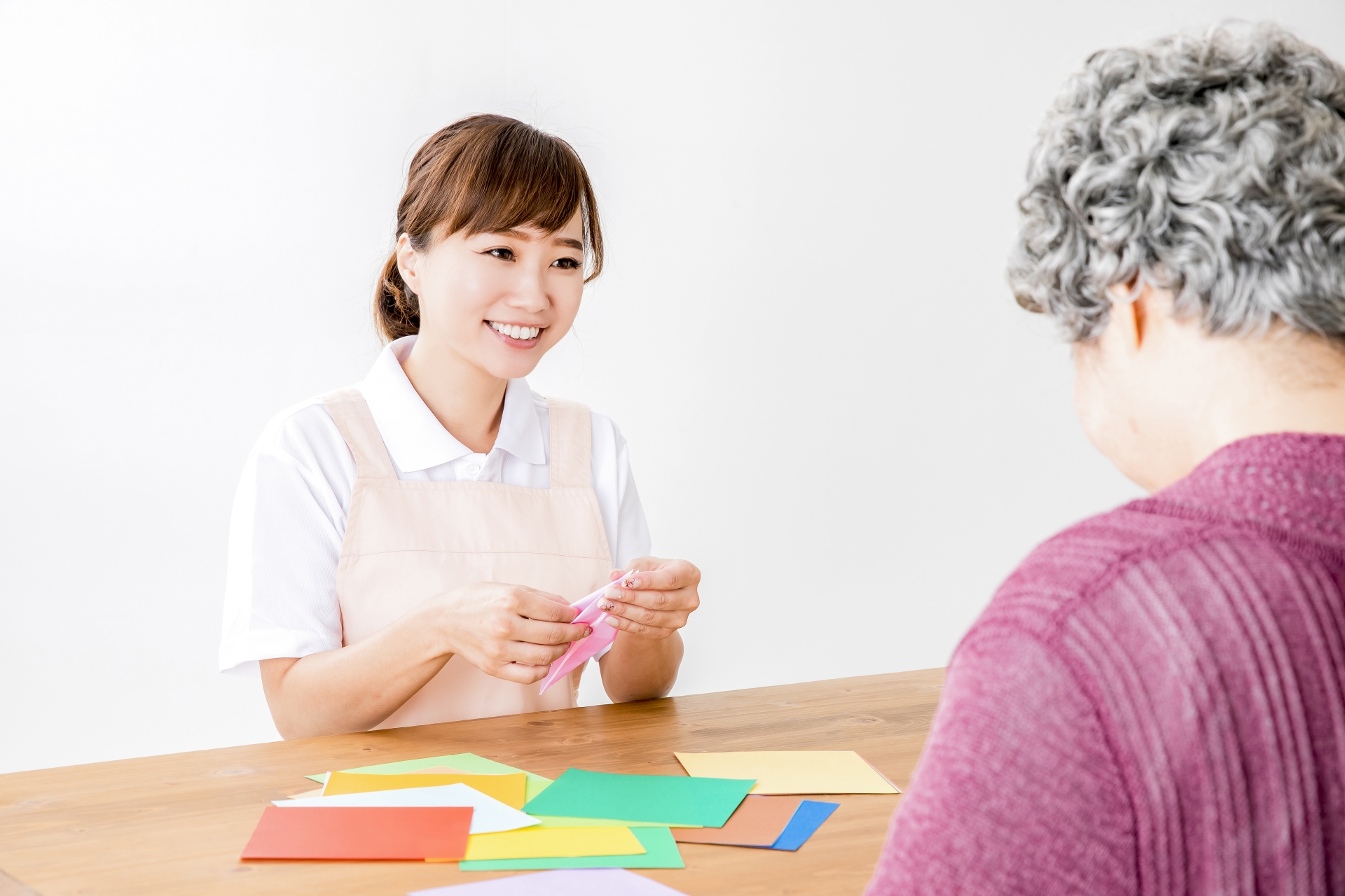 折り紙でレクリエーションする介護士と高齢者の女性