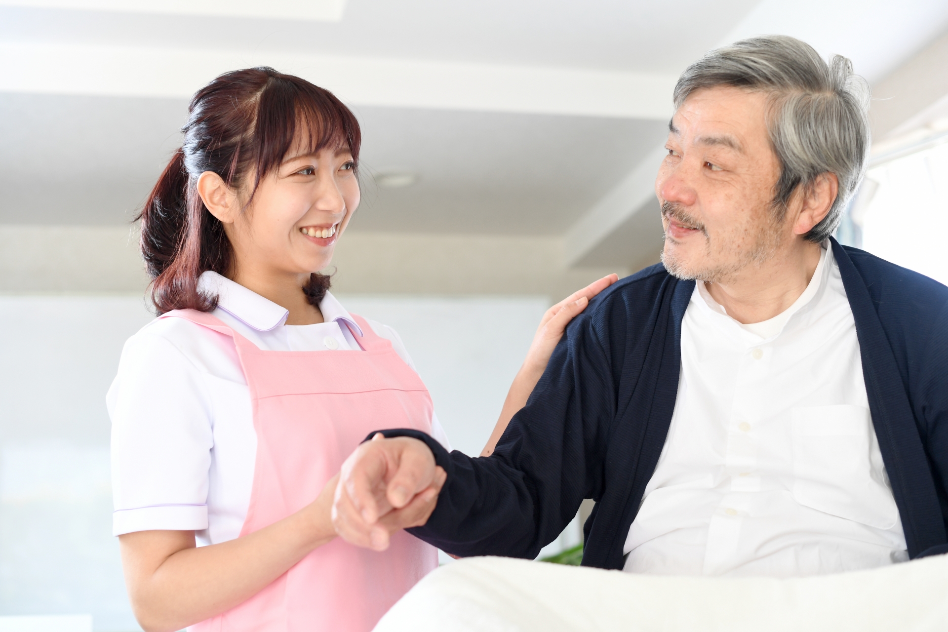 ベッドで寝たきりのお年寄りと介護士の女性
