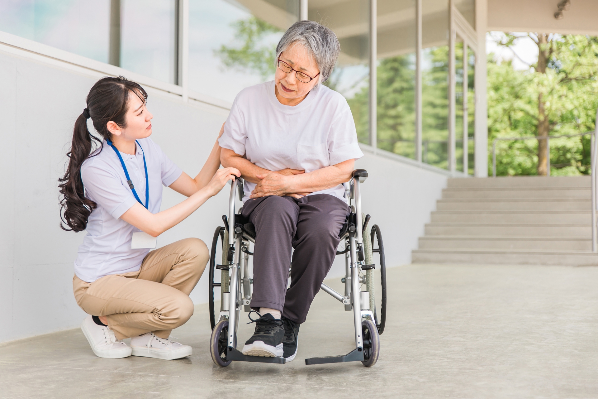 介護士とお腹をおさえる車椅子に乗る高齢者
