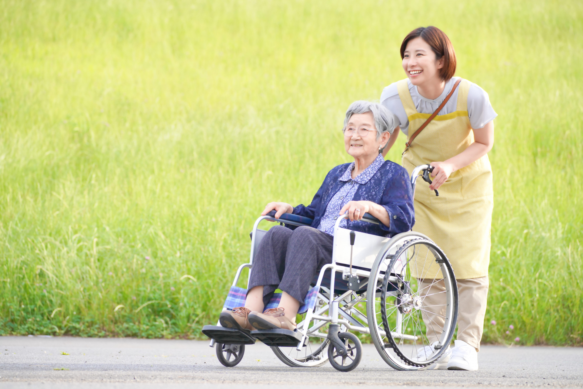 車椅子を押すヘルパーと高齢者
