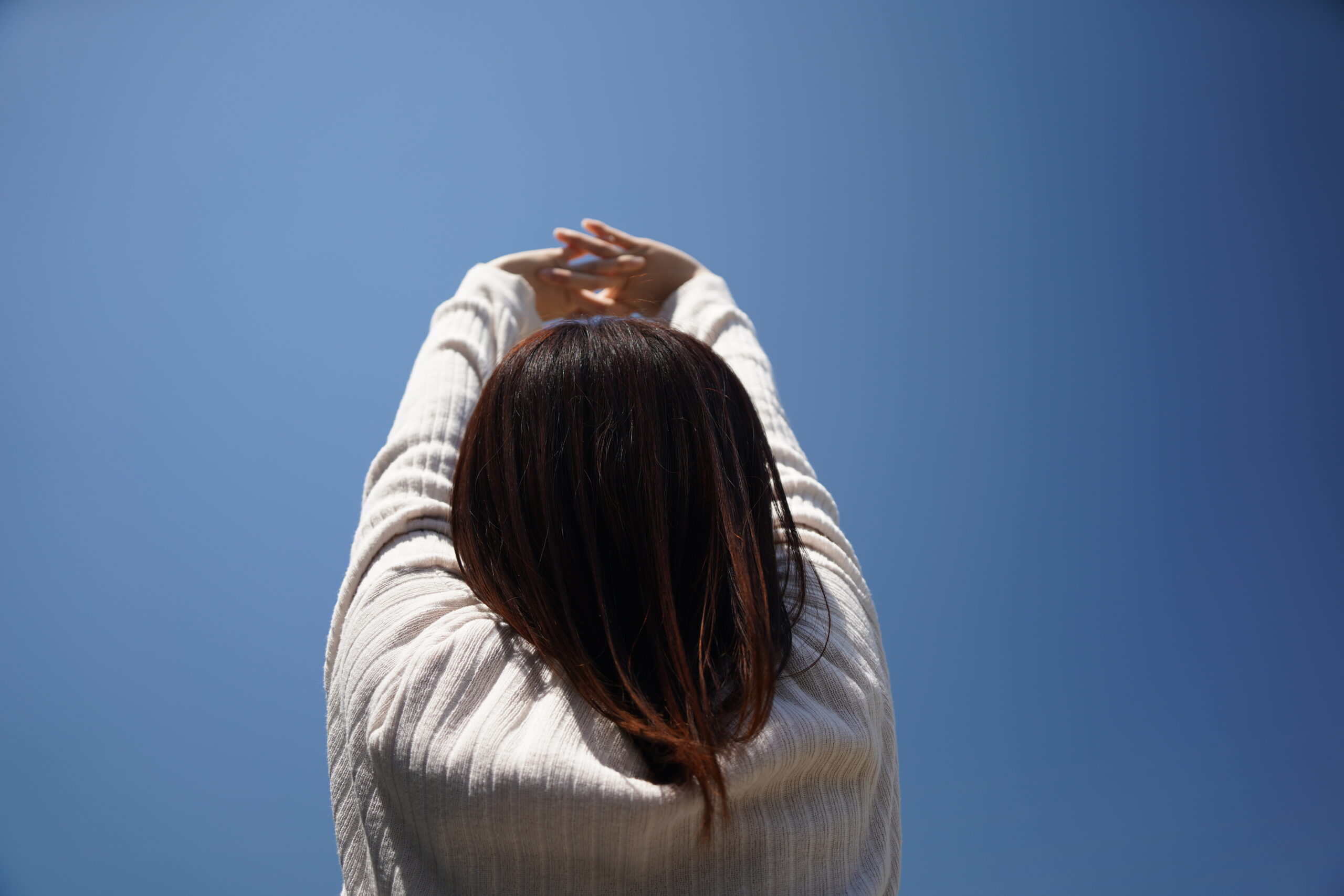 青空に向かって深呼吸をする女性