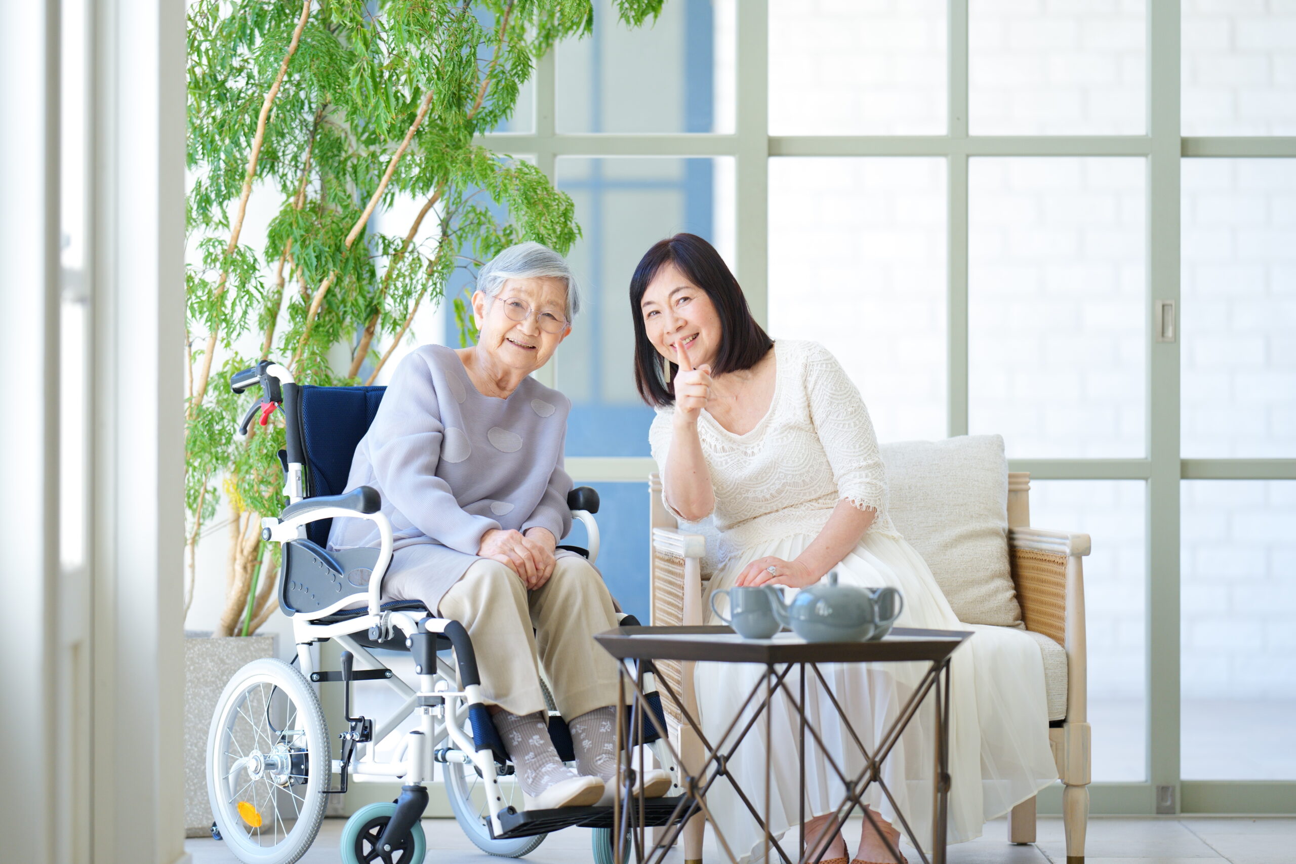 車椅子に乗っている高齢女性とソファに座る娘