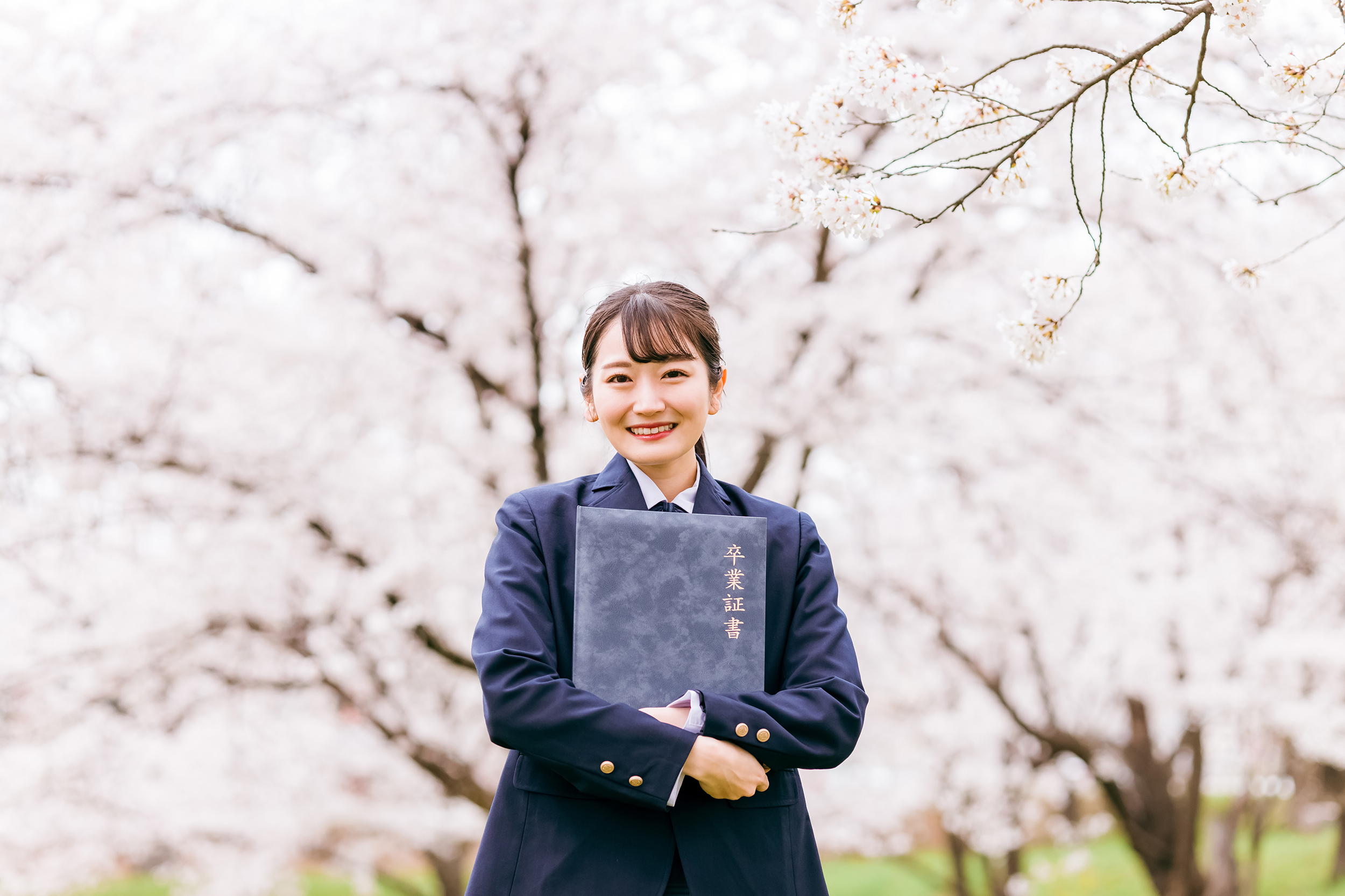 満開の桜の下で卒業証書を持つ高校生