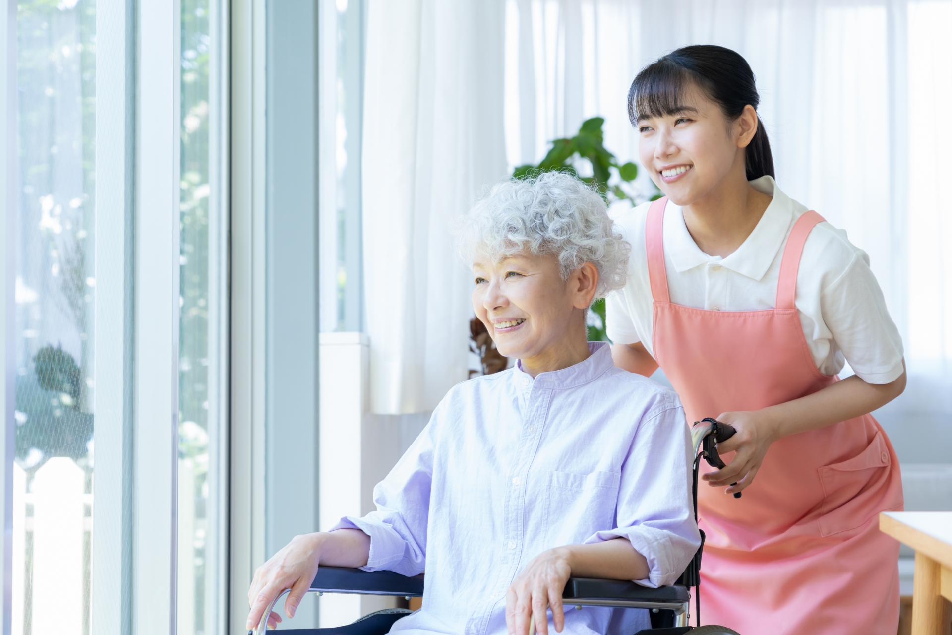 車椅子を支えるピンクのエプロンの介護職員
