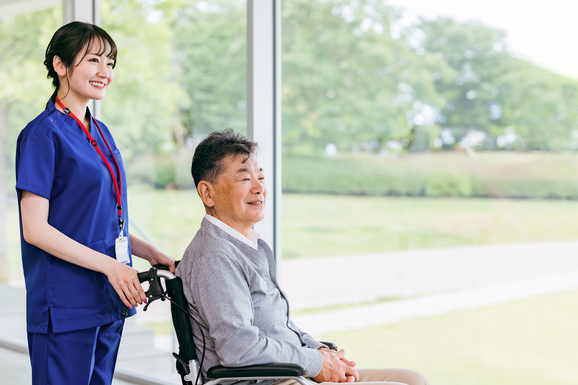 窓のそばに立つ車椅子の男性と介護士
