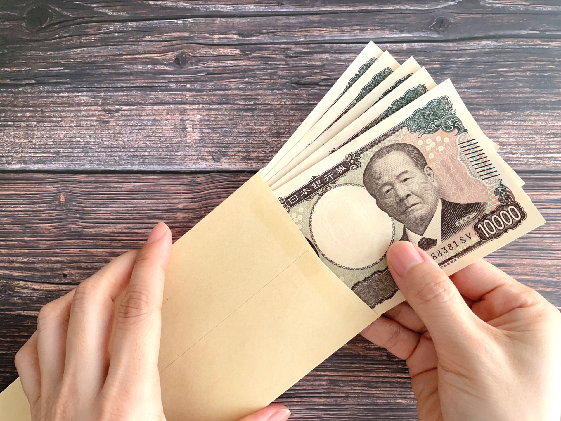 茶封筒に入った5万円を持つ女性の手元