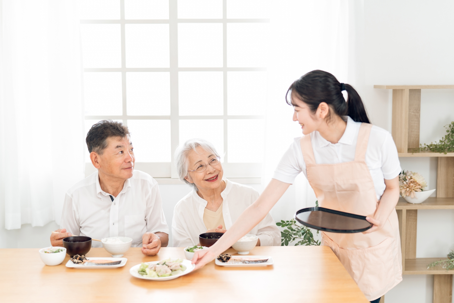 お食事を提供する介護士と高齢夫婦