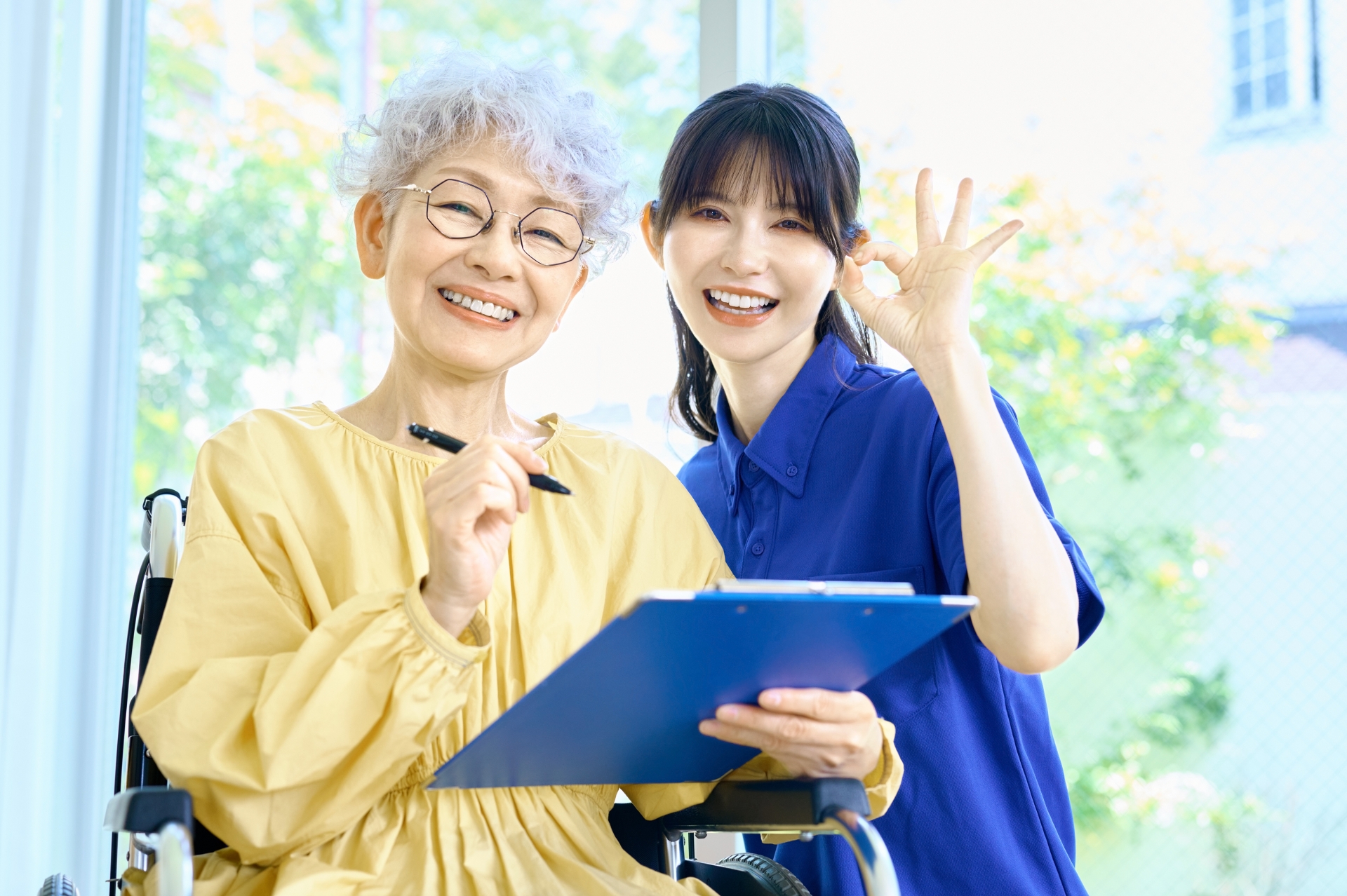 OKサインをする介護士とペンを持つ車椅子の女性