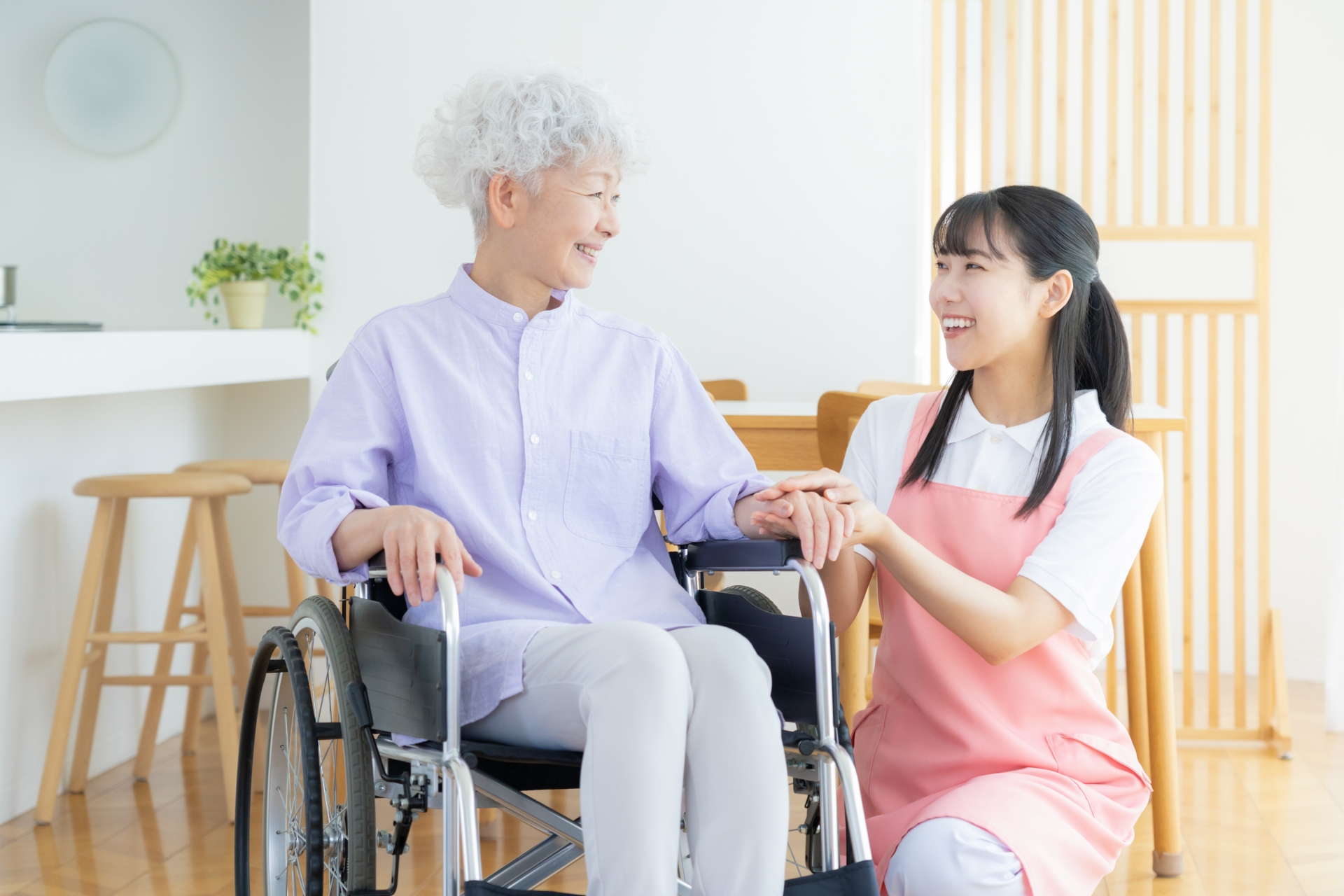 会話するピンクのエプロンの介護士と車椅子の女性