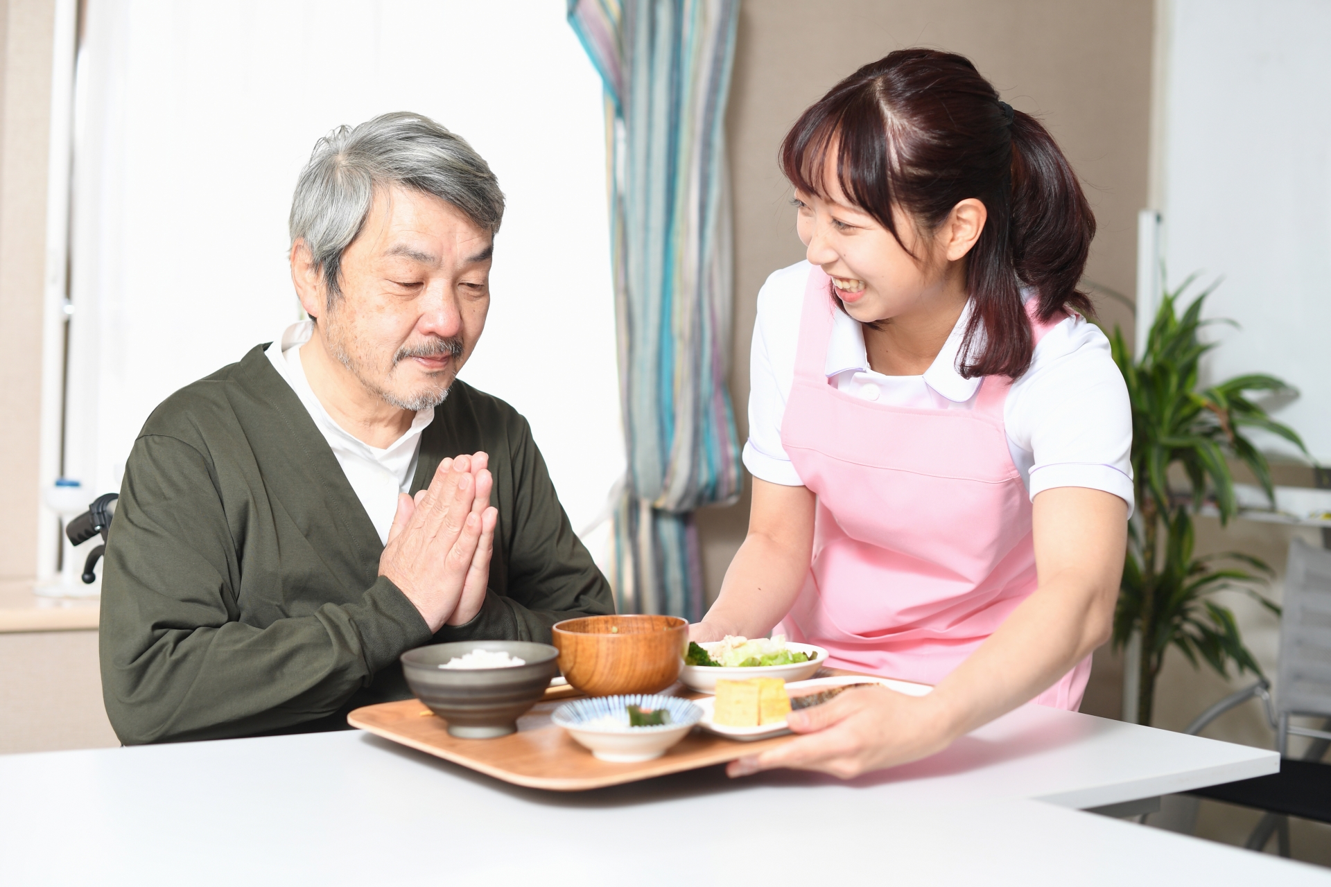 食事の配膳をする女性介護士と高齢者男性