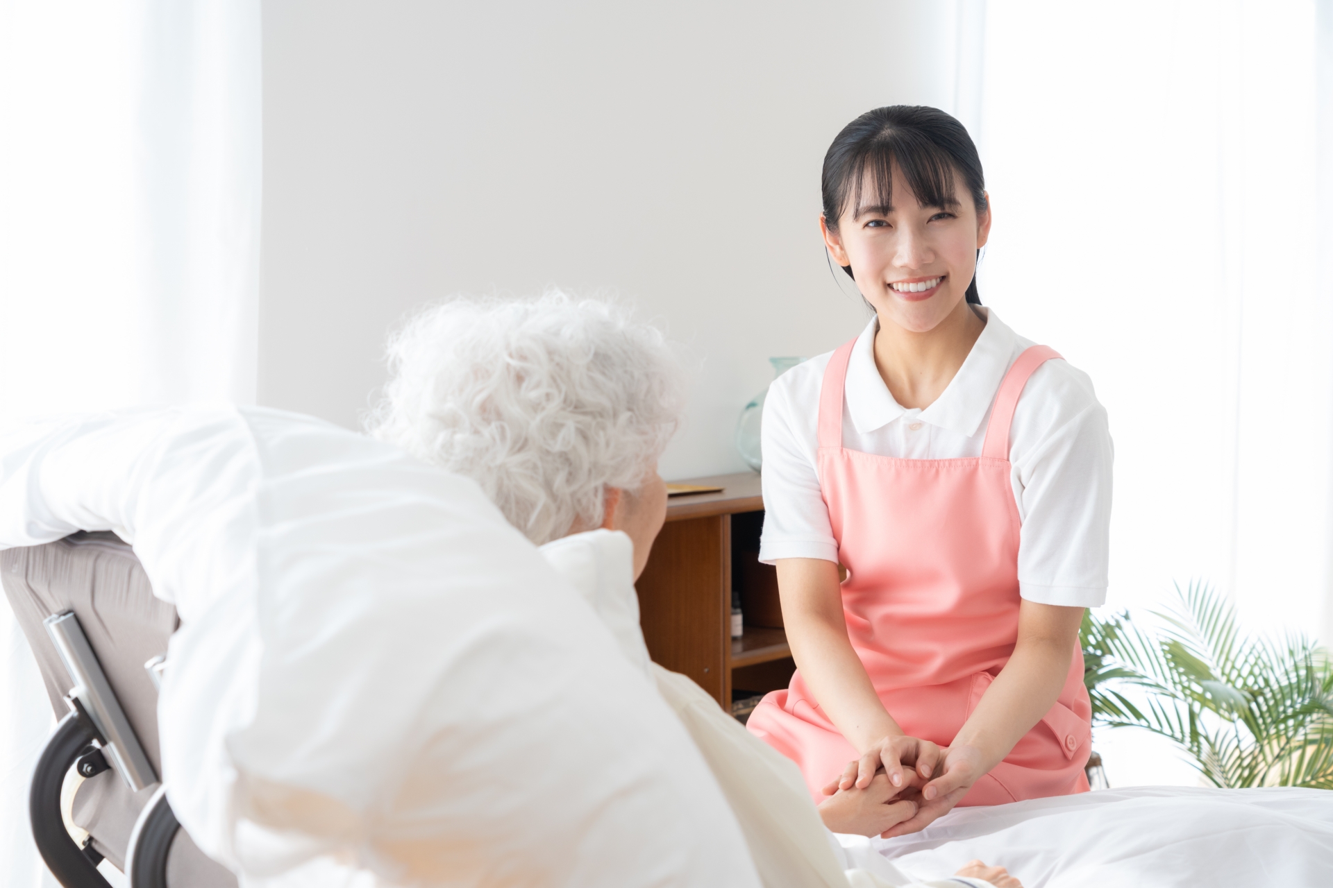 寝ているシニア女性を介護をする介護士