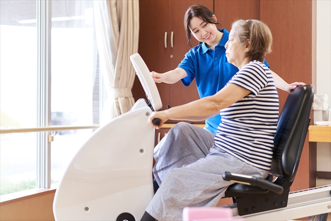 バイクで運動をする高齢者と見守る介護士