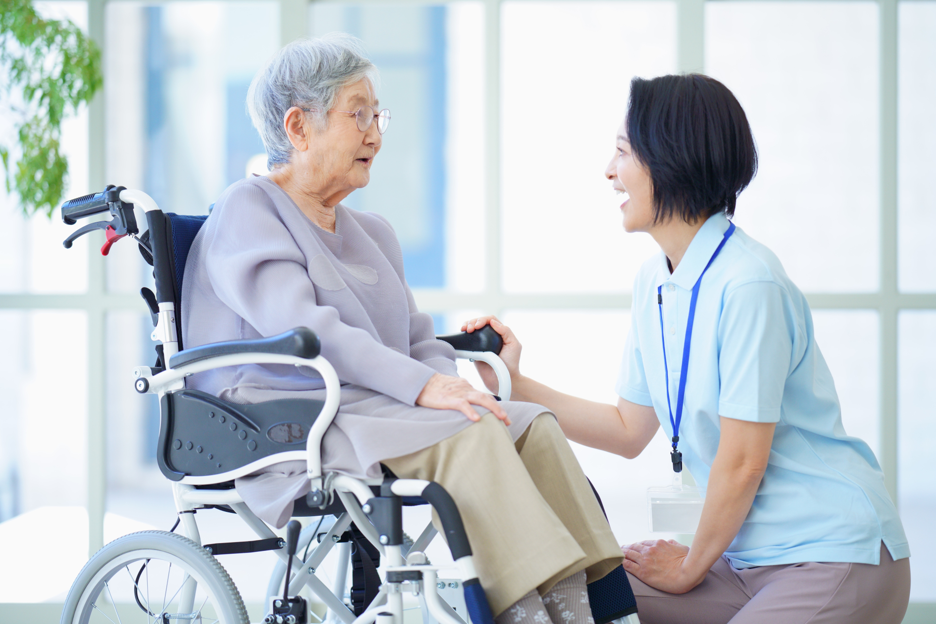 車椅子に乗っている高齢女性に話しかける介護士