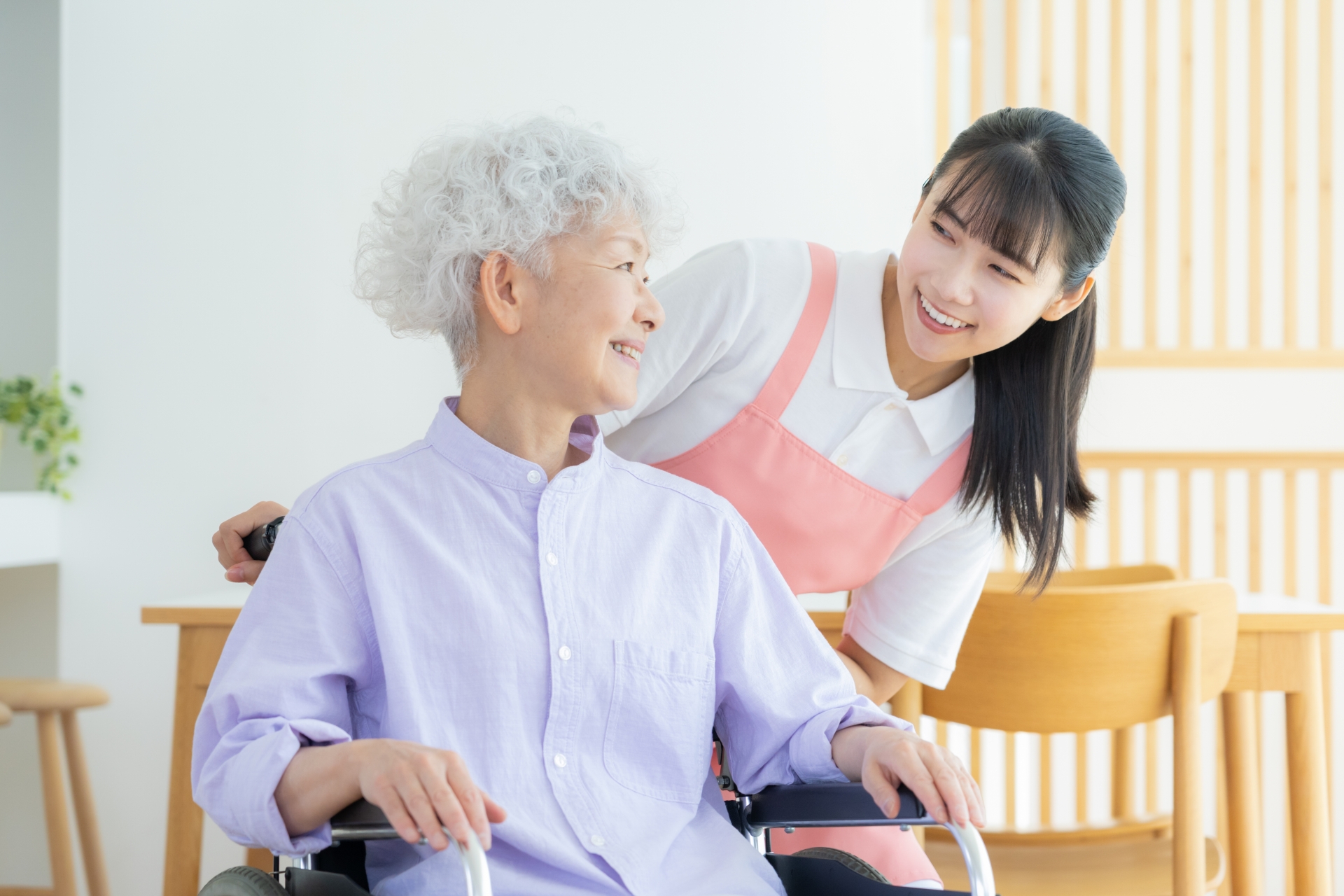 車椅子の女性の背後から声をかける介護士