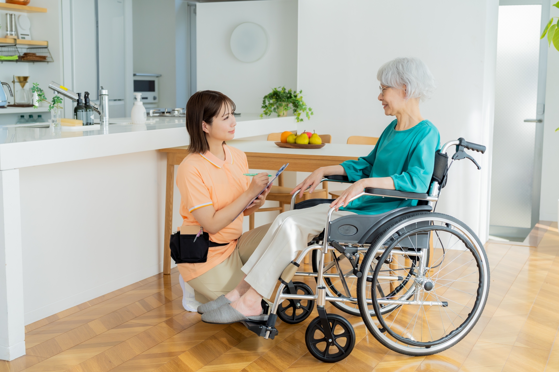 かがんで車椅子の女性と話す介護士