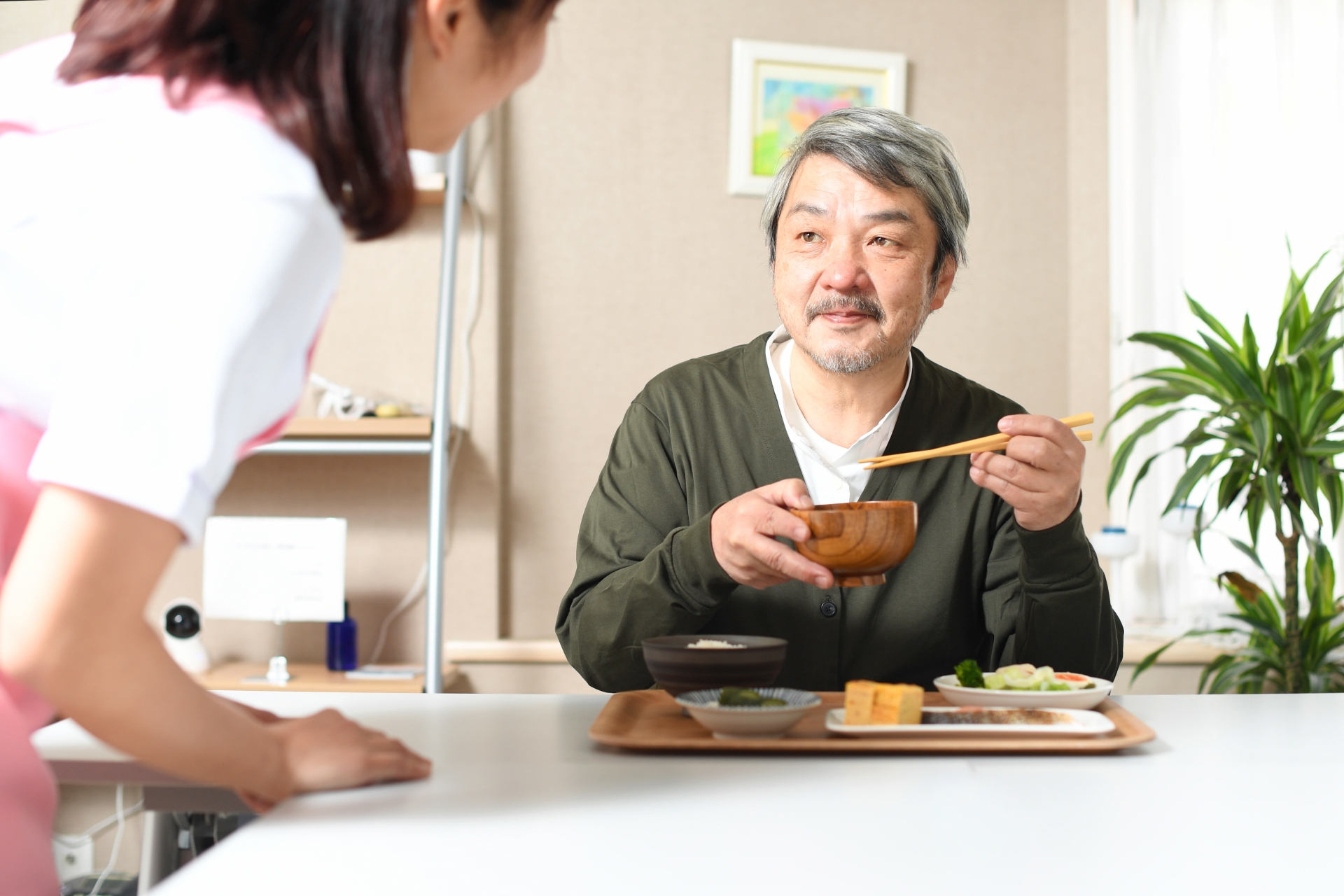 食事を運ぶ女性介護士と高齢者の白髪男性