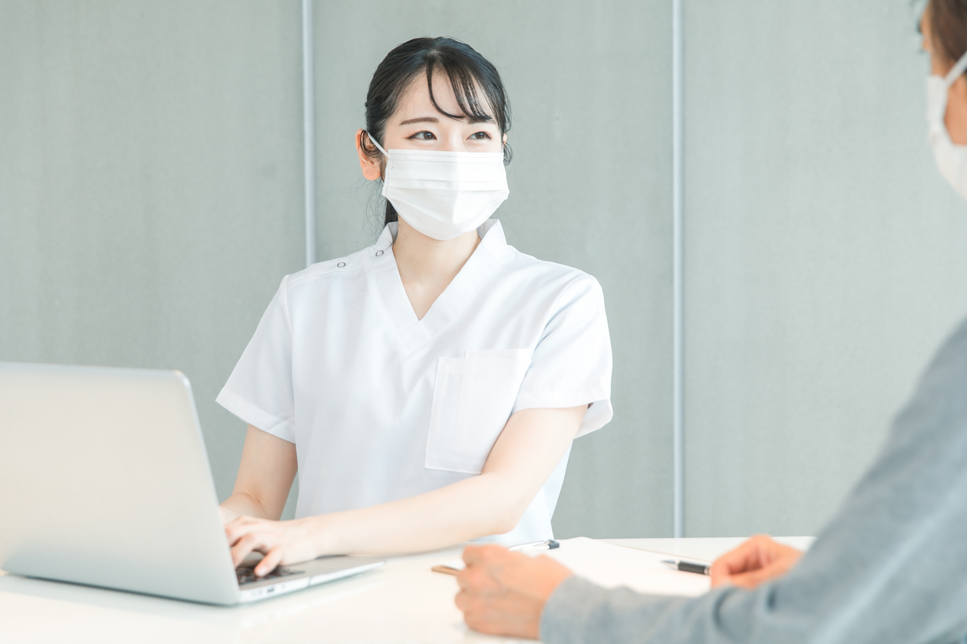 パソコンで受付する白衣の女性と患者