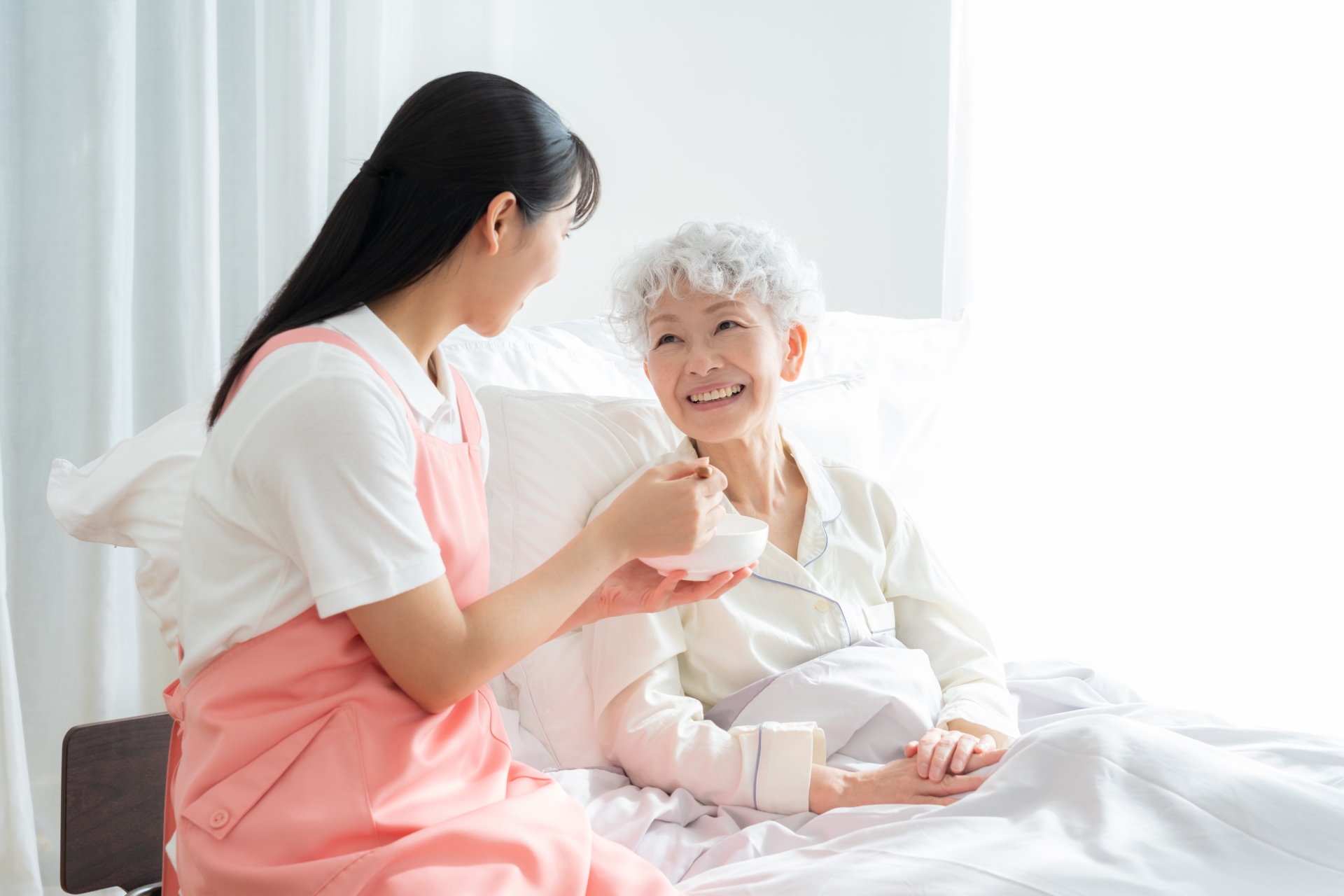 寝ているシニア女性を介護をする介護士