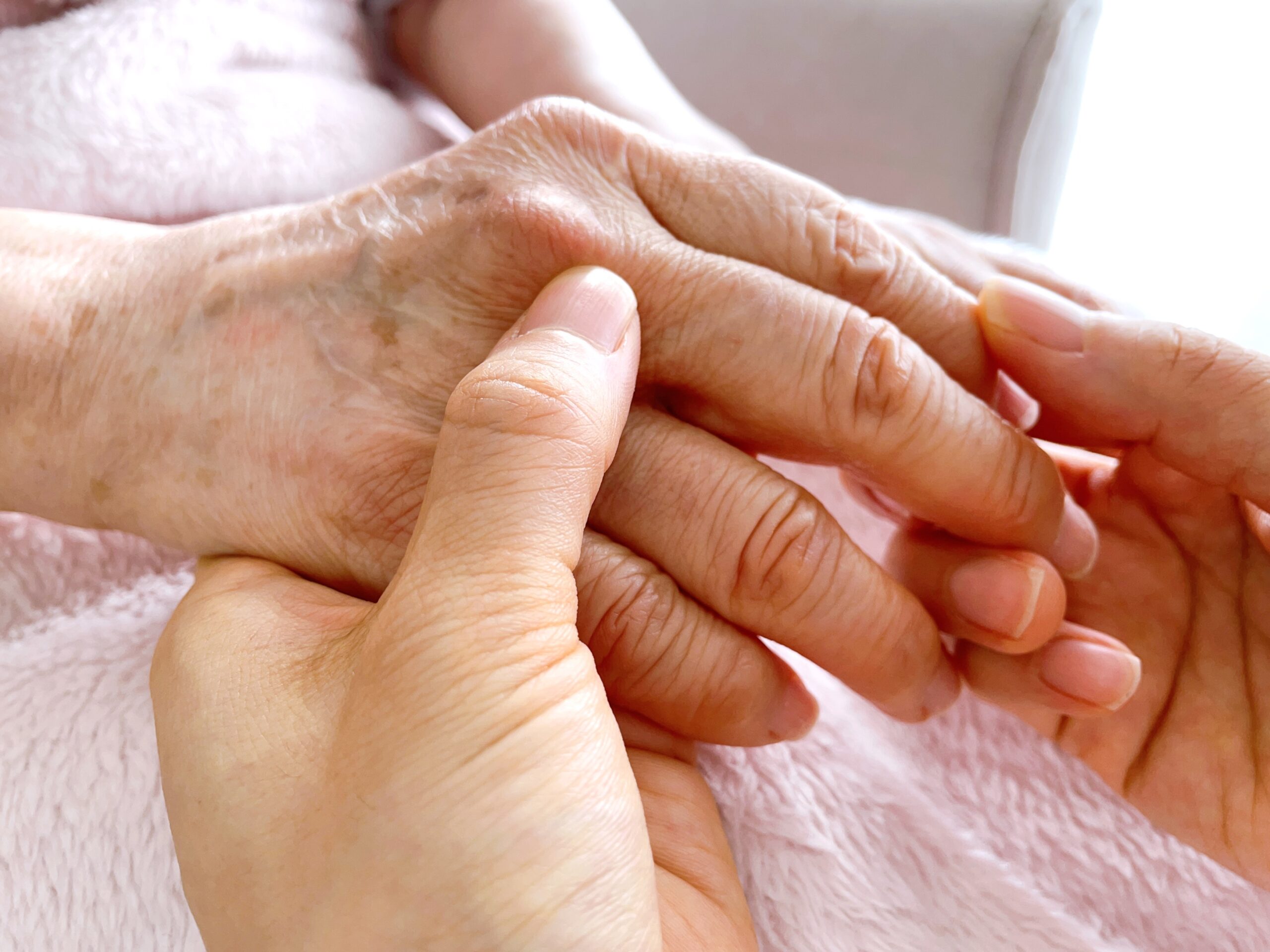 高齢女性の手をマッサージする女性の手元