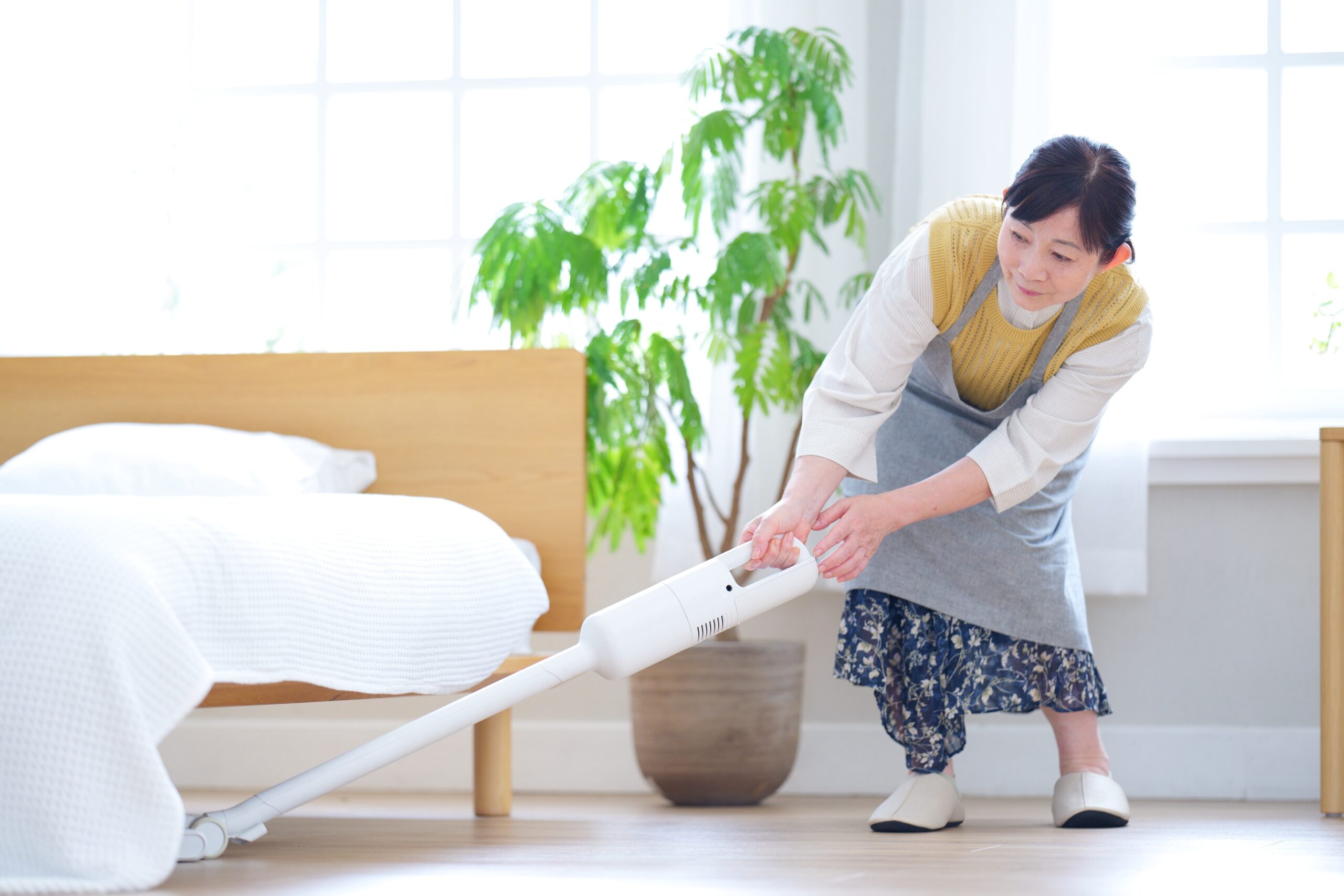ベッド下を真剣に掃除するエプロン姿の女性