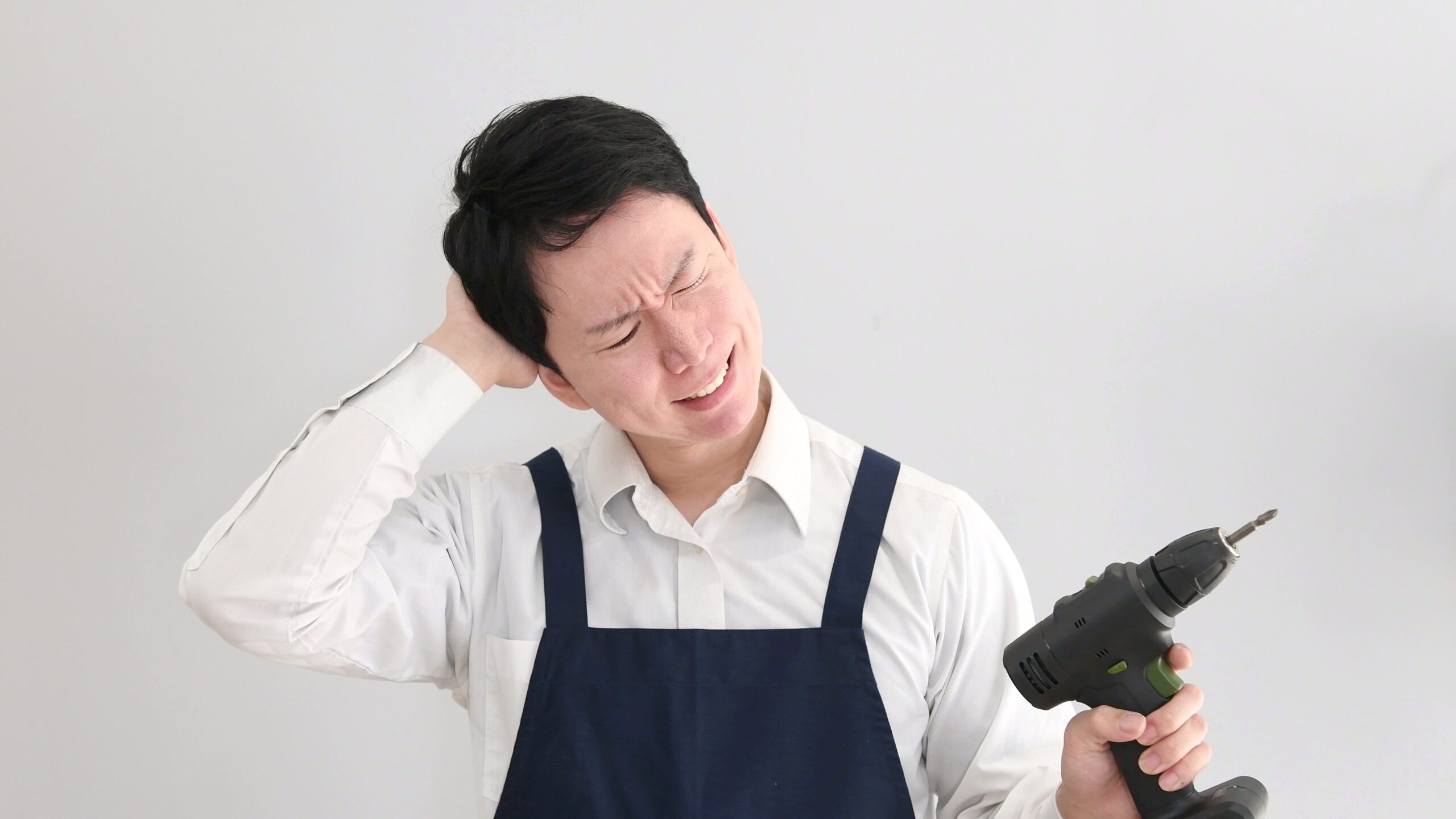 電動ドリルを持ちながら困るエプロンの男性