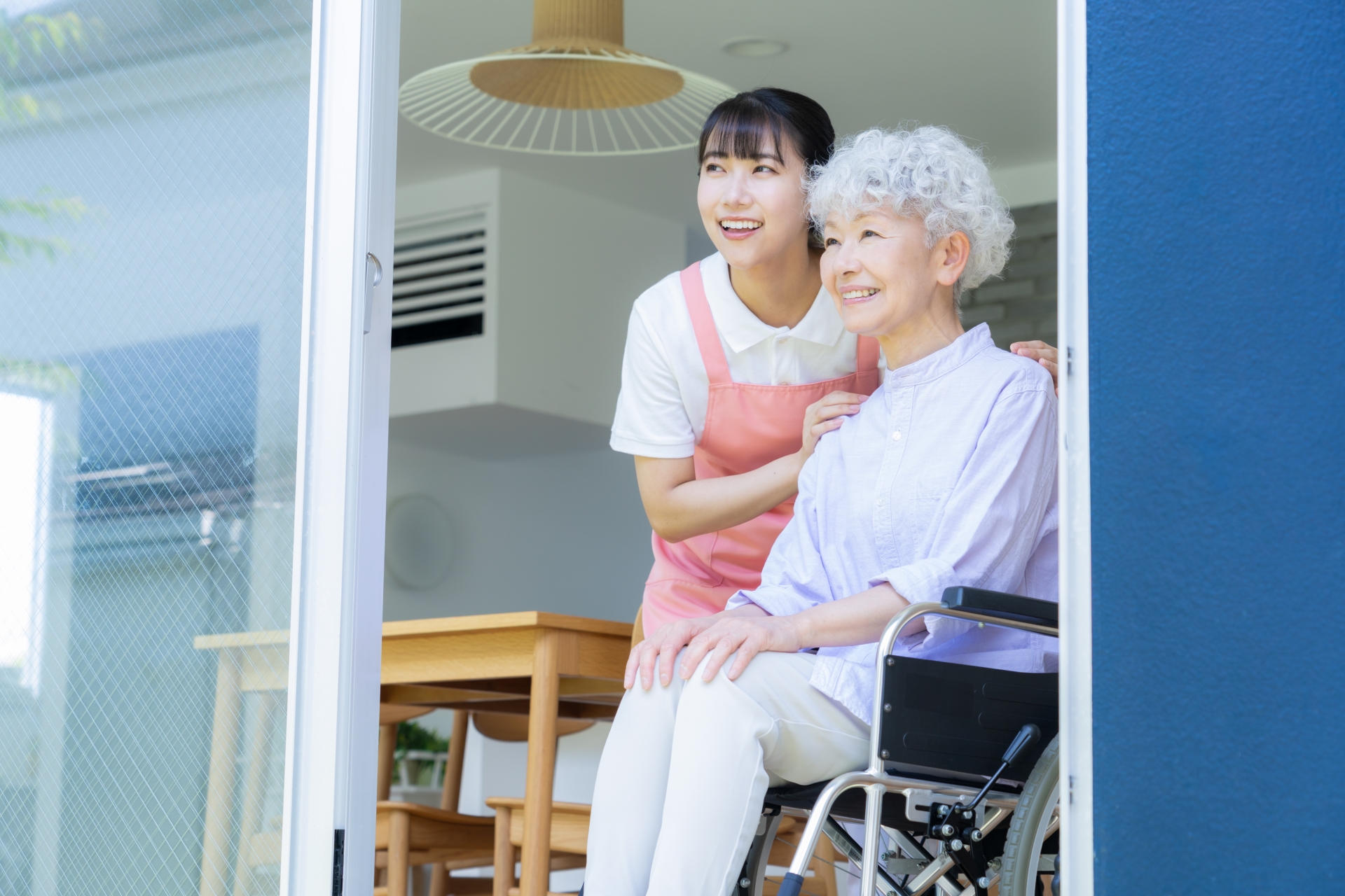 窓際でシニア女性を介護をする介護士の女性