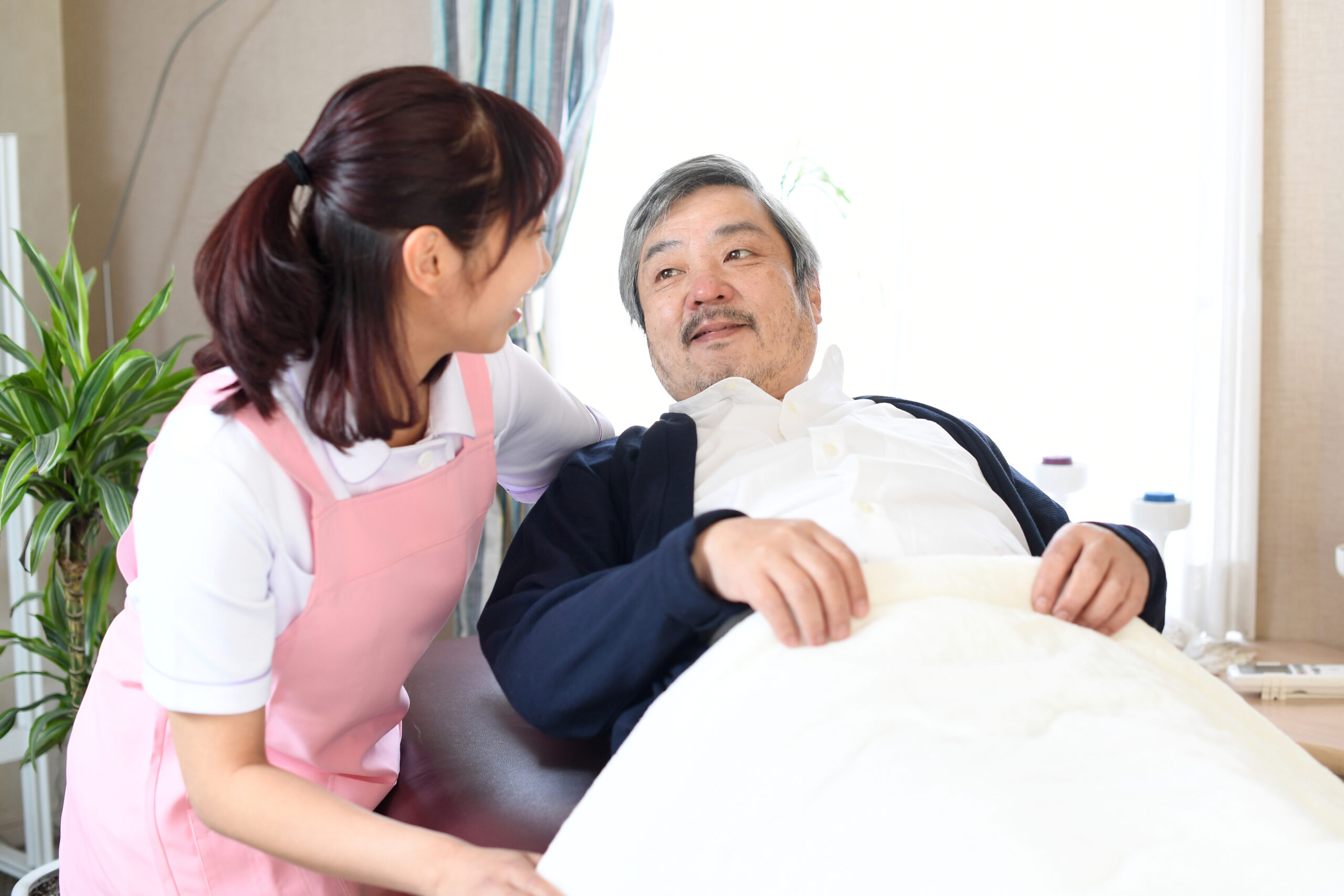 ベッドで寝たきりのお年寄りと介護士の女性