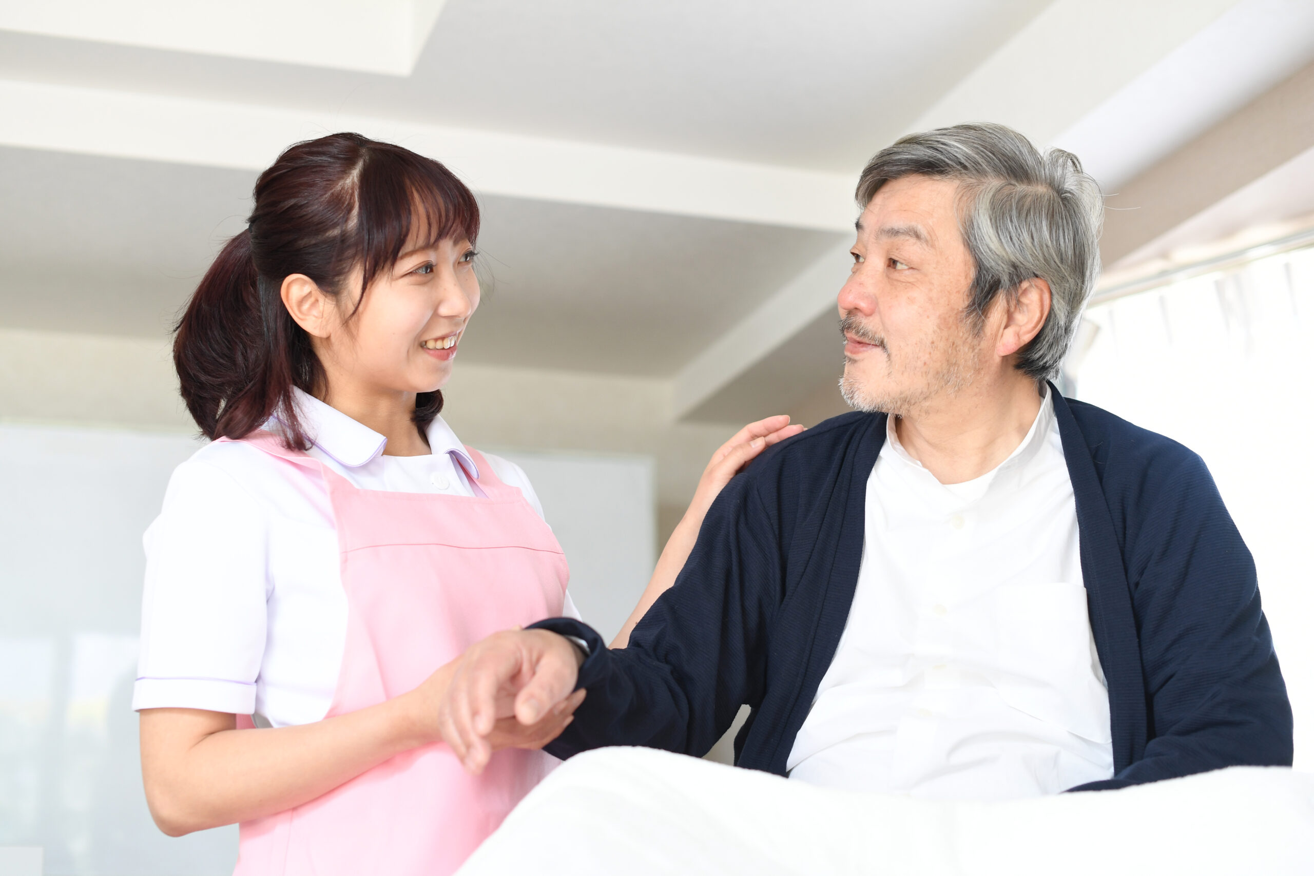 ベッドで寝たきりのお年寄りと介護士の女性