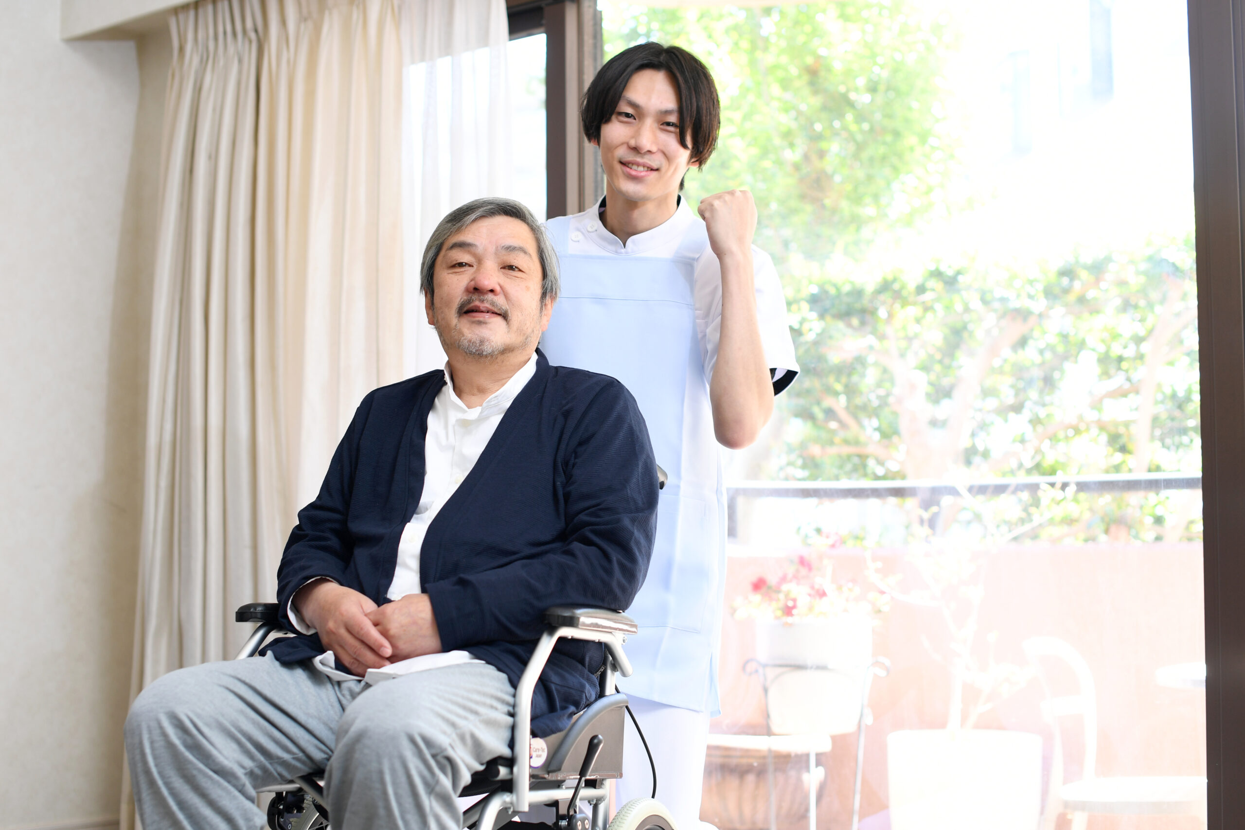 車椅子に乗る高齢者男性とガッツポーズをする男性介護士