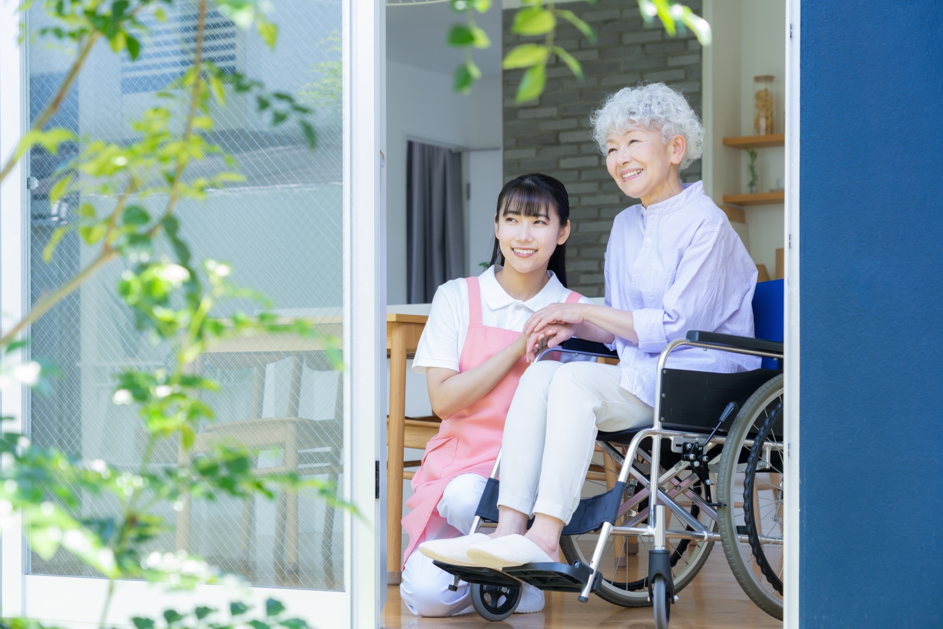 窓際でシニア女性を介護をする介護士の女性