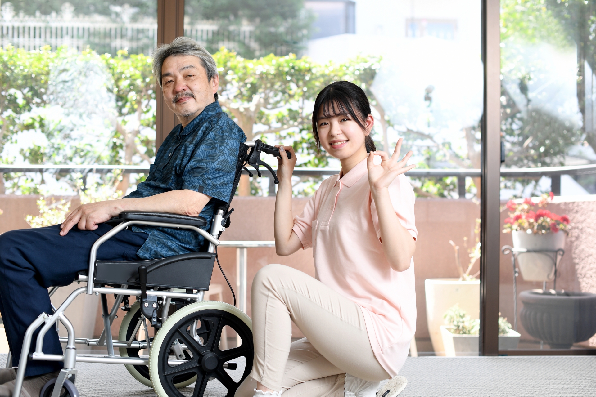 車椅子の男性とOKサインをする介護士