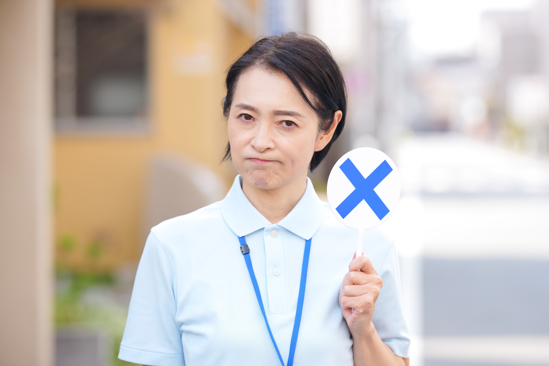 屋外でバツの札を見せる女性介護士