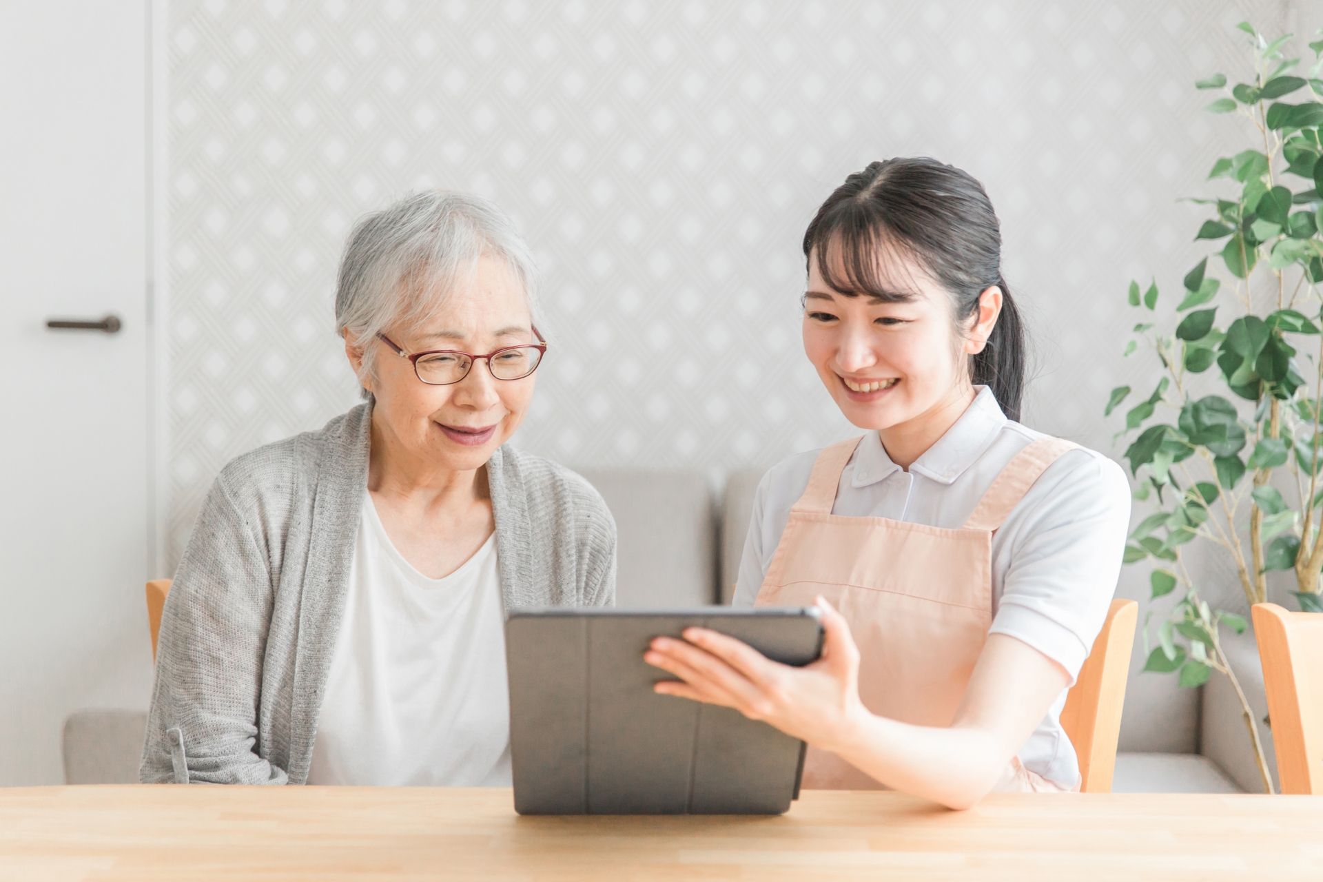 タブレットを使うエプロン姿の女性と高齢者女性