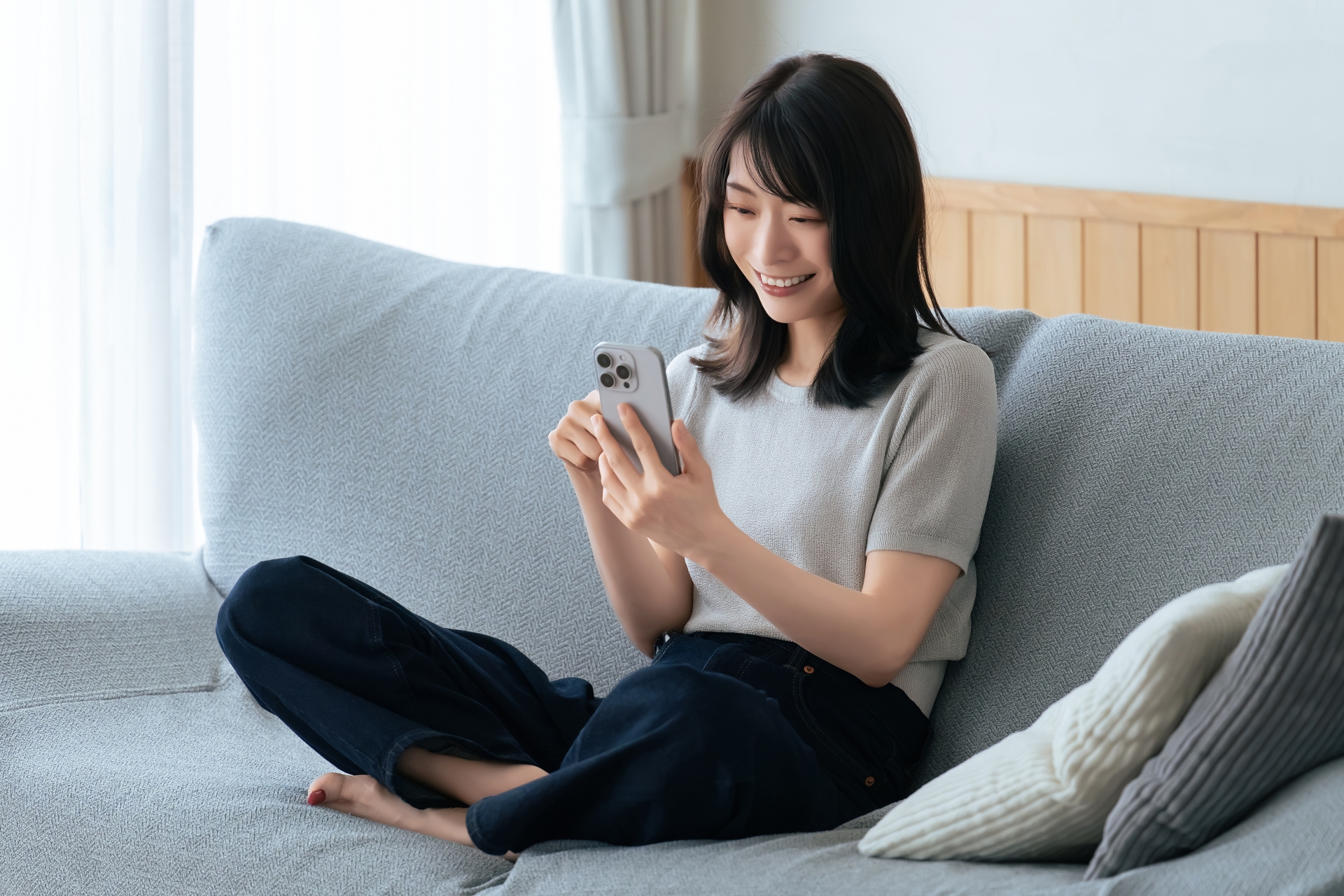 ソファに座ってスマホを使う笑顔の女性