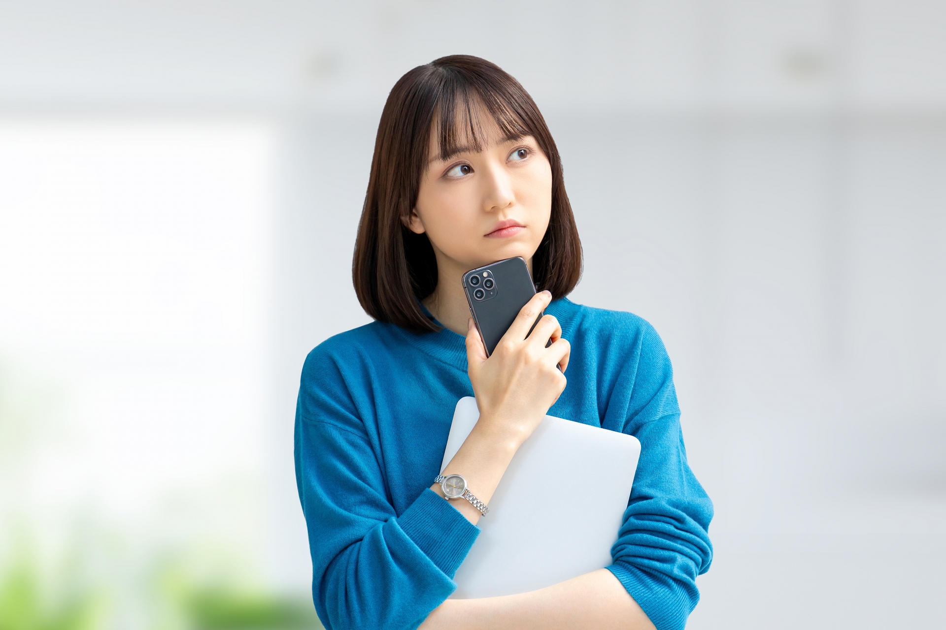 スマホとパソコンを持って考える女性