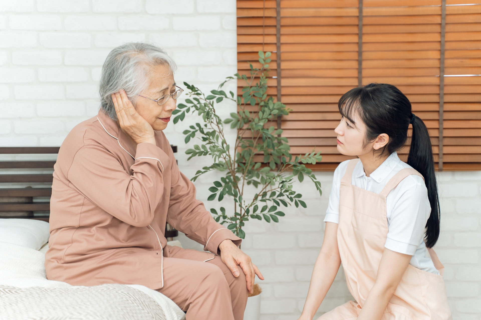 痛がる高齢者女性とエプロン姿の女性（耳）