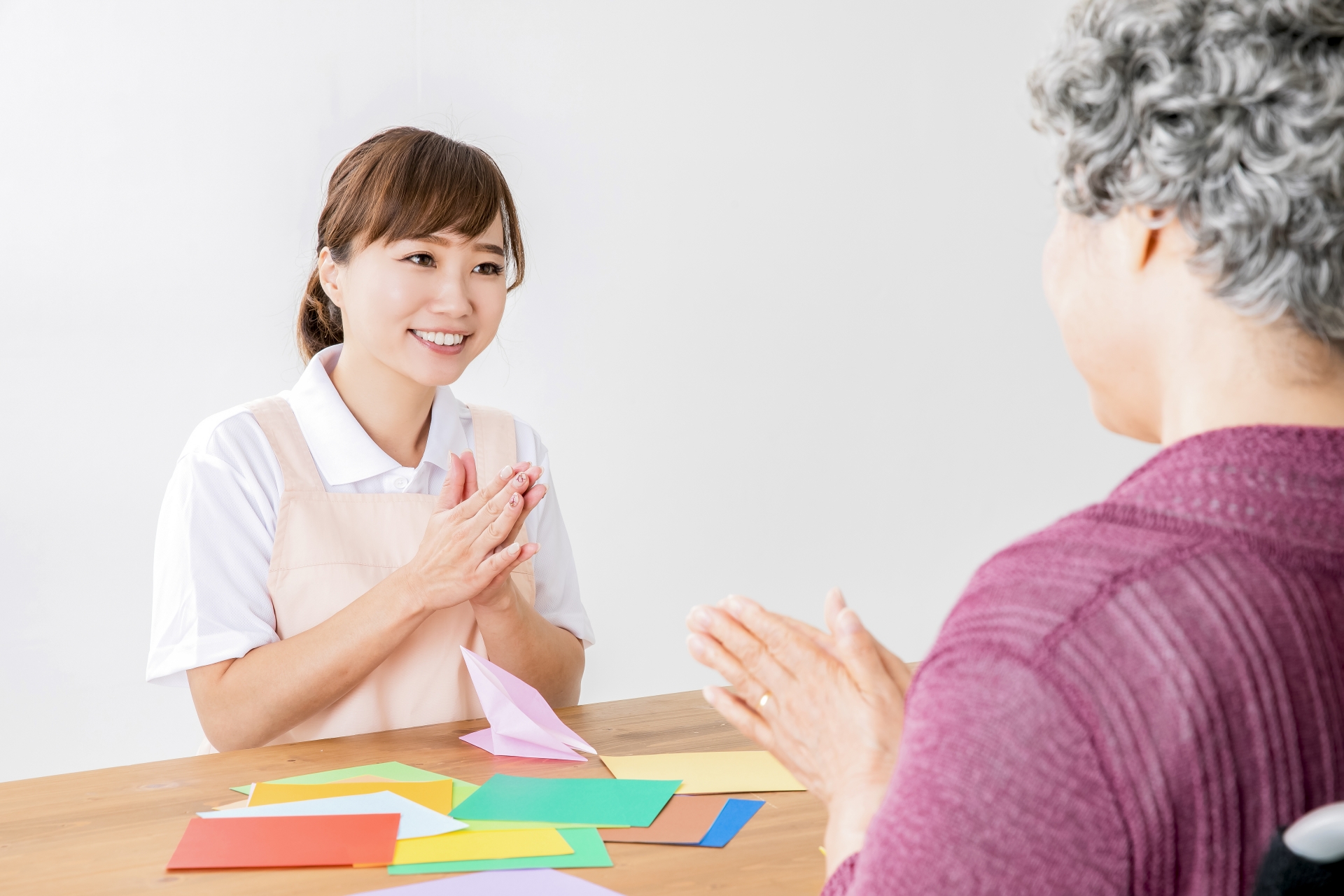 折り紙する高齢者を褒める介護士
