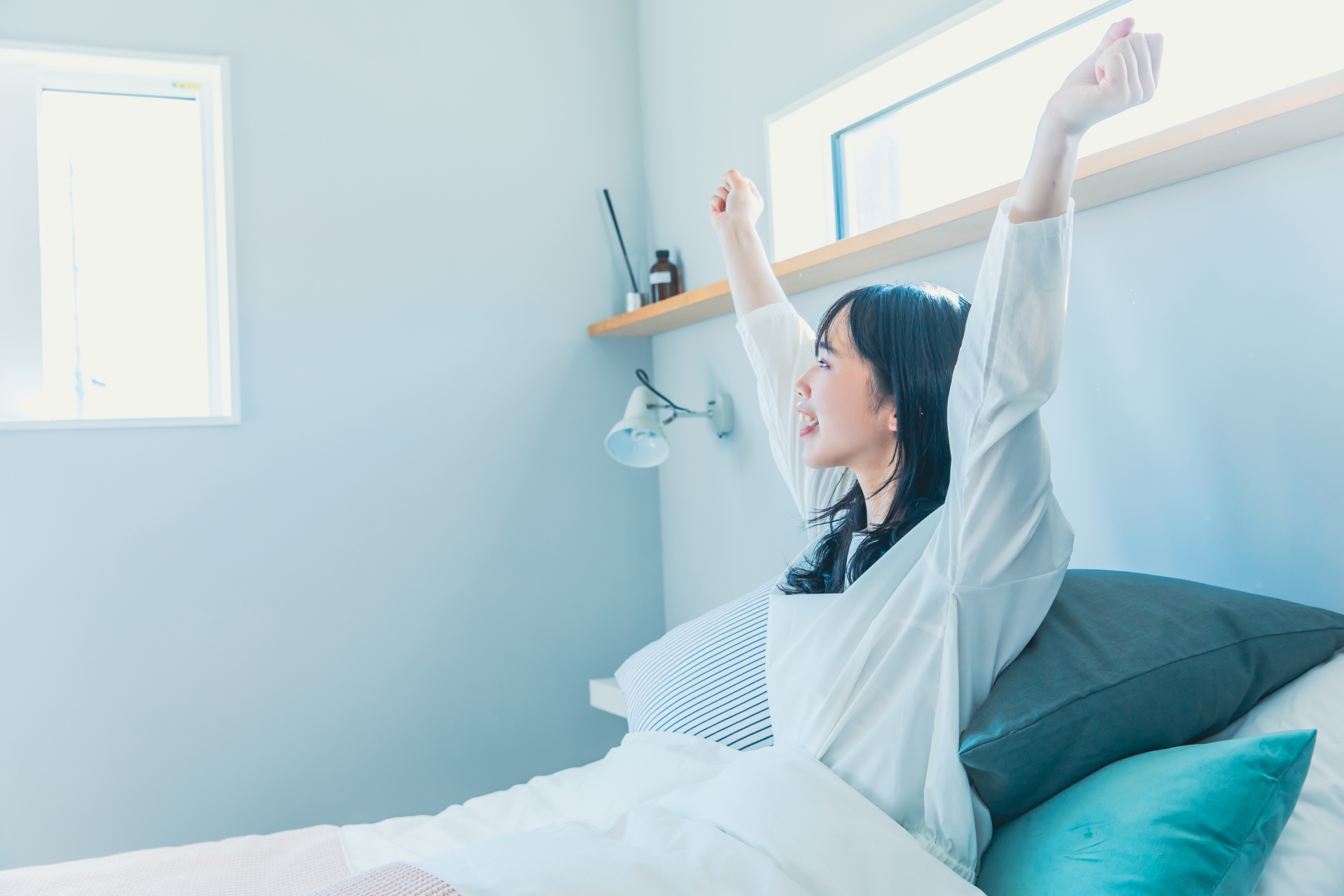 ベッドの上で両腕を伸ばす女性