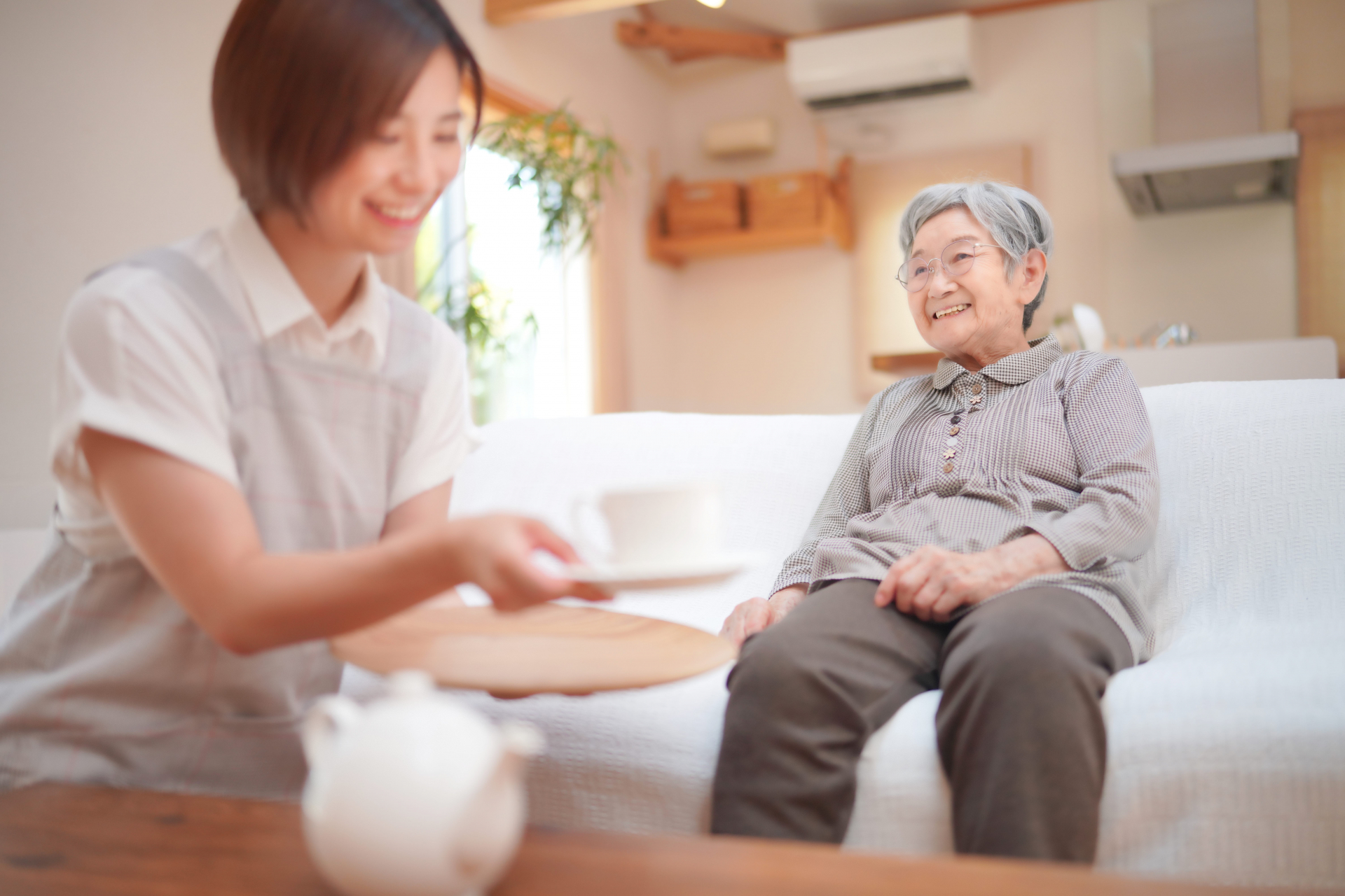 ソファに座る高齢女性にお茶を出す介護士