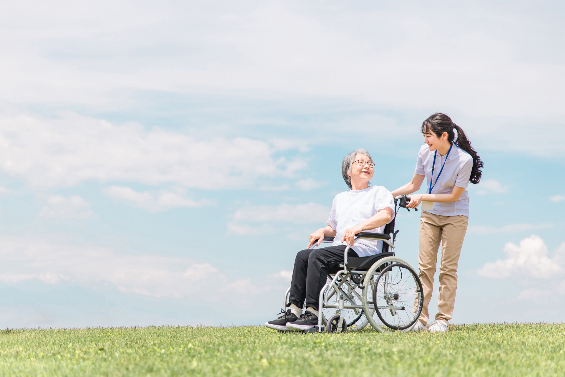 公園を散歩する介護士と車椅子の高齢者女性