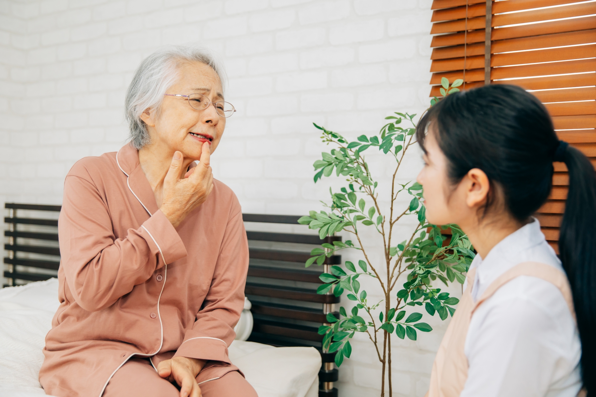 痛がる高齢者女性とエプロン姿の女性