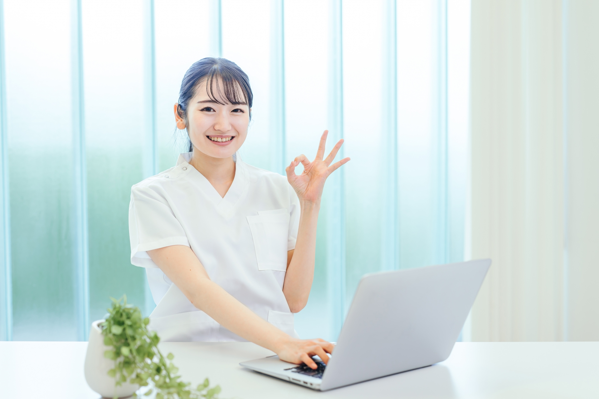 パソコンの前でOKサインをする白衣の女性