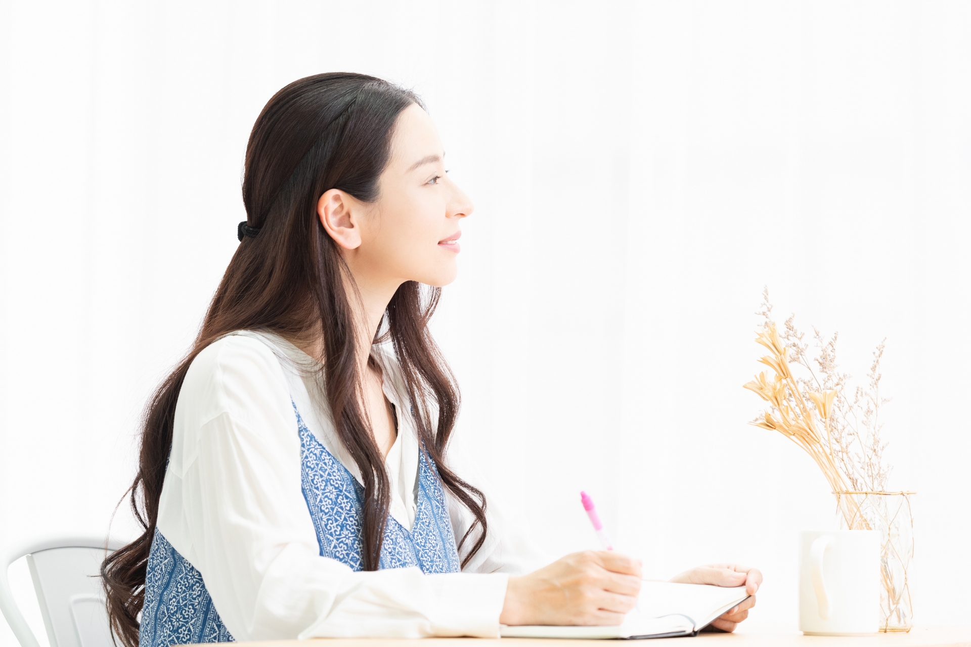 リビングで座りながら手帳にメモを書く主婦